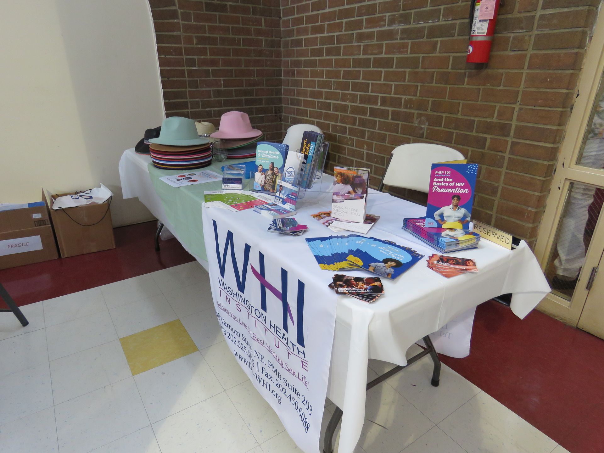 Table with information and hats, in front of a brick wall, likely a community event.