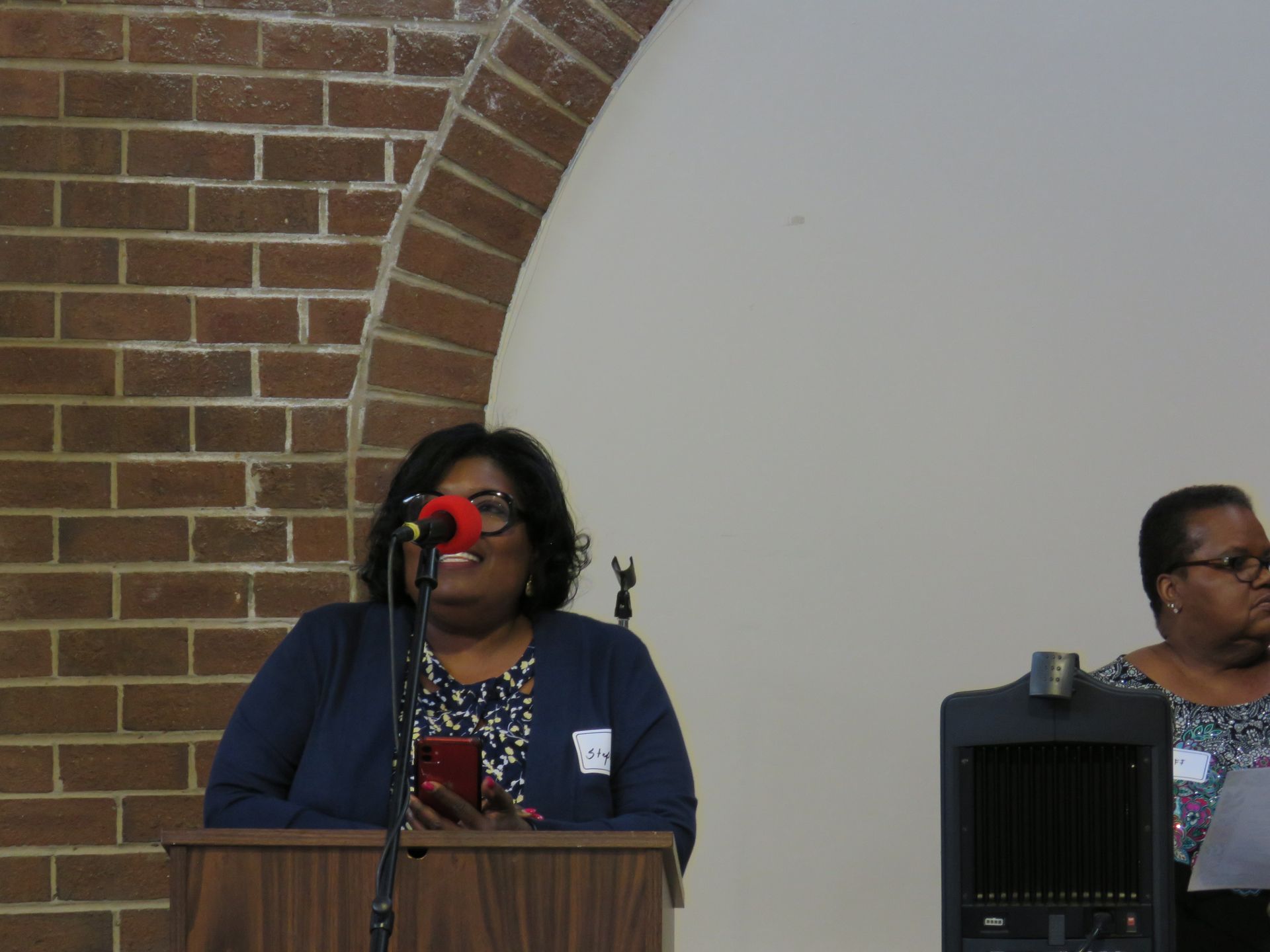Woman speaking at podium, brick wall backdrop.