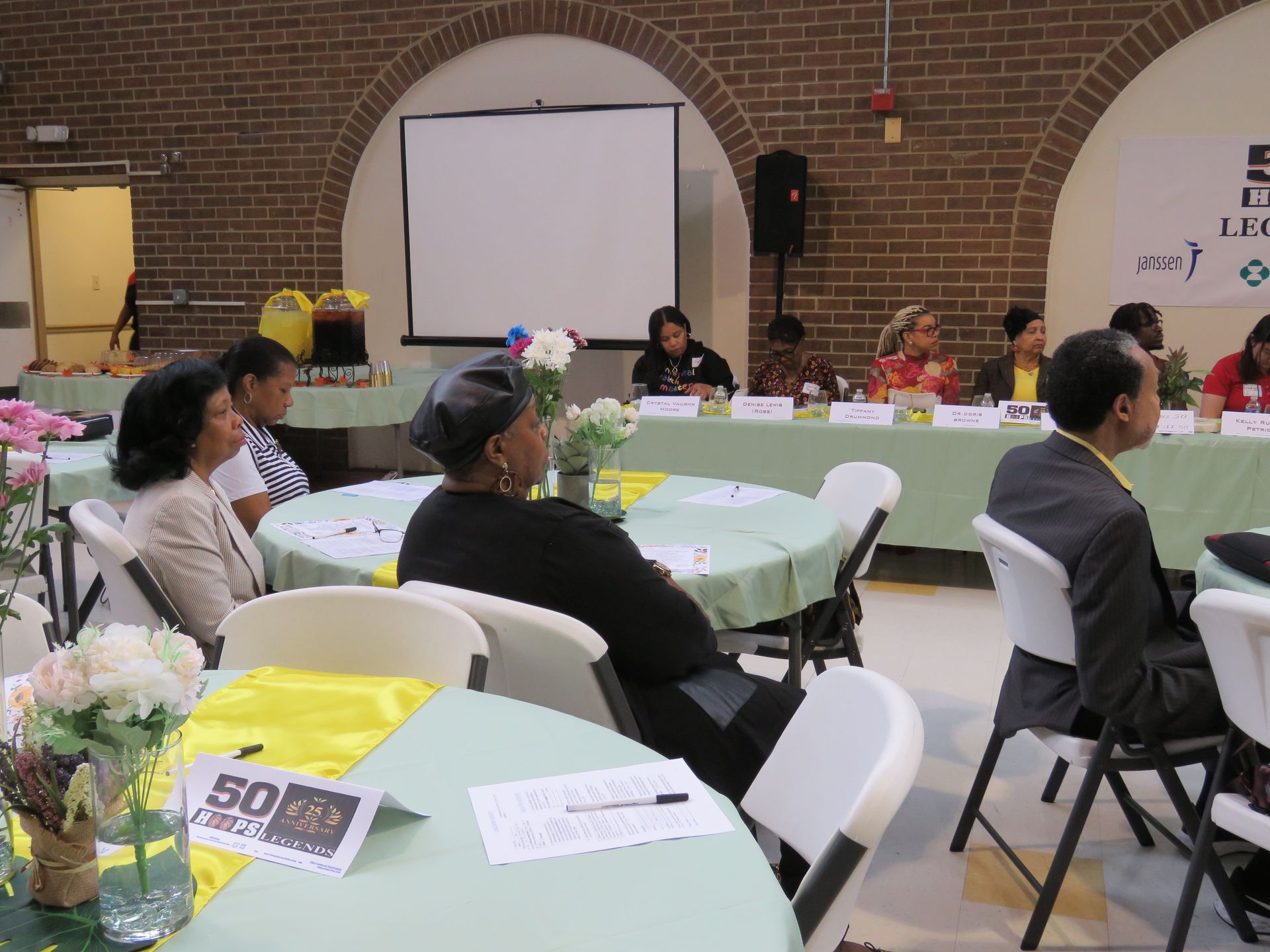 People at tables in a room with a panel seated in the background.