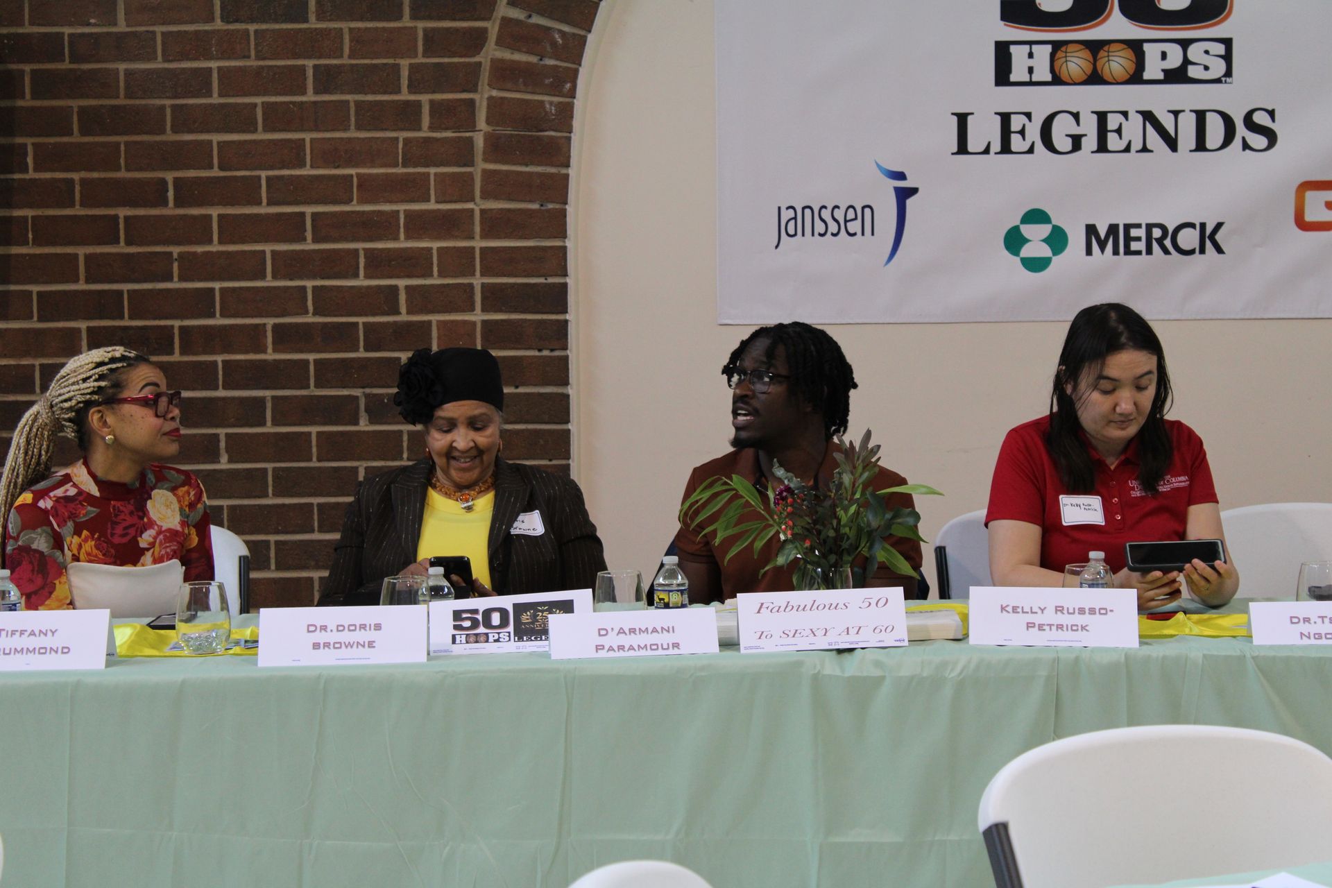 Panel discussion with four people at a table; logo for 