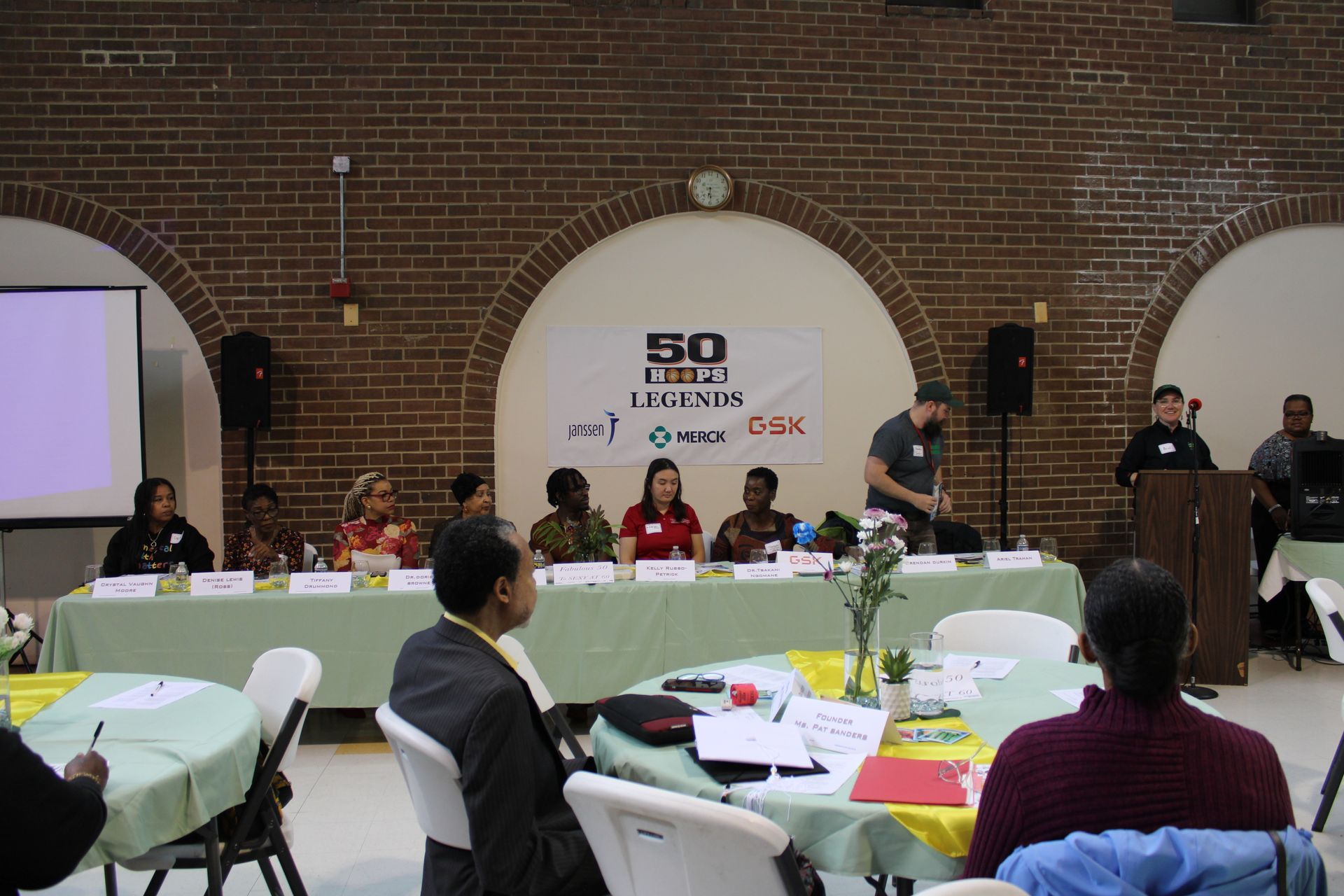 Panel discussion with speakers at a table, attendees in foreground, banner reading 