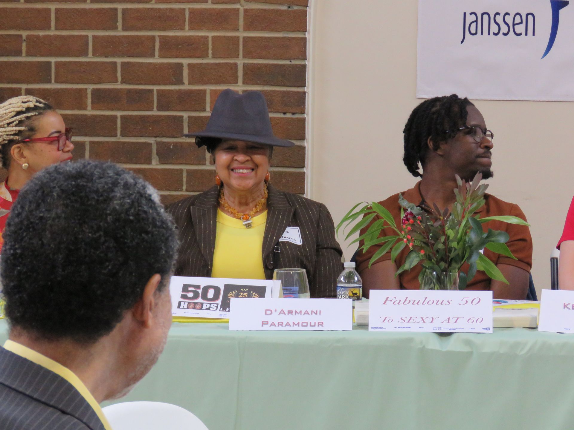 Panel of people at a table; brick wall background. Speakers smiling, a sign reading Janssen.