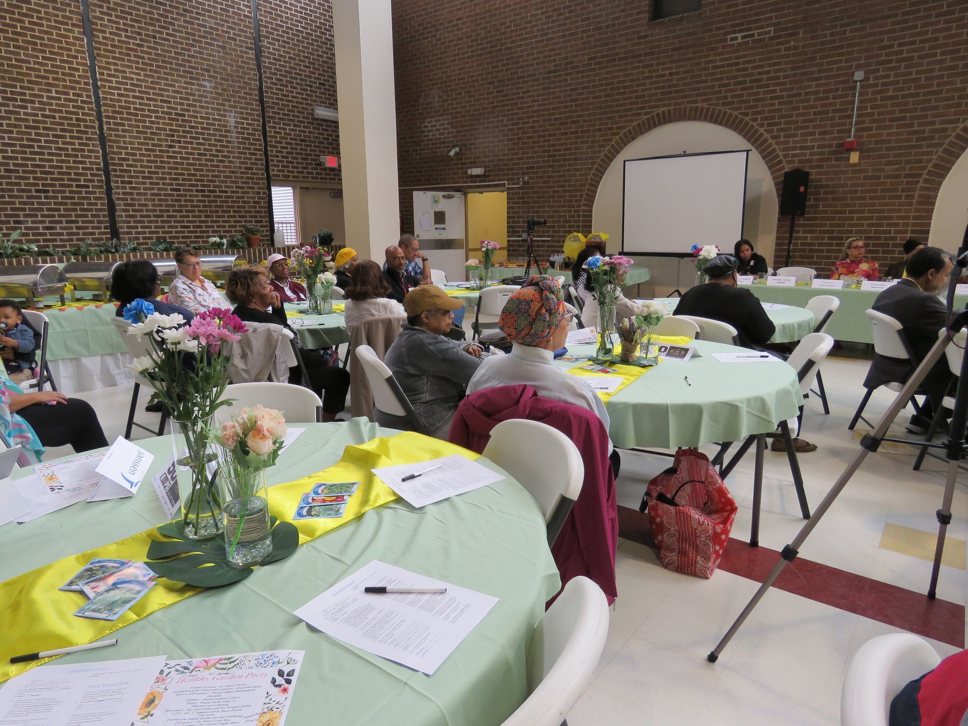 People seated at round tables in a large hall, likely an event or meeting.