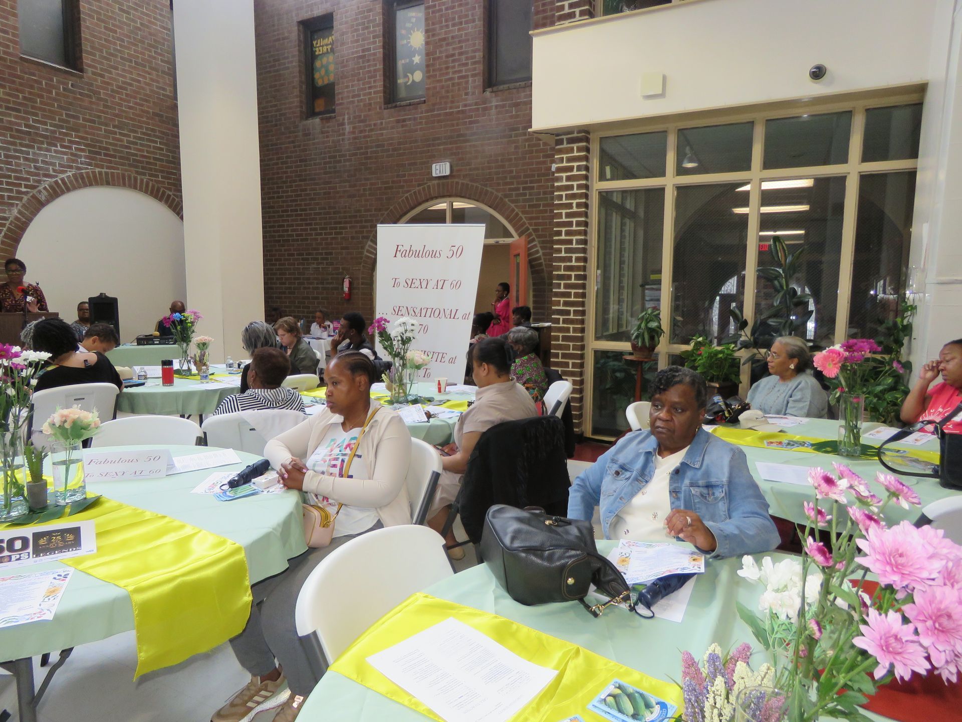 People seated at round tables decorated with flowers, in a brick-walled room.