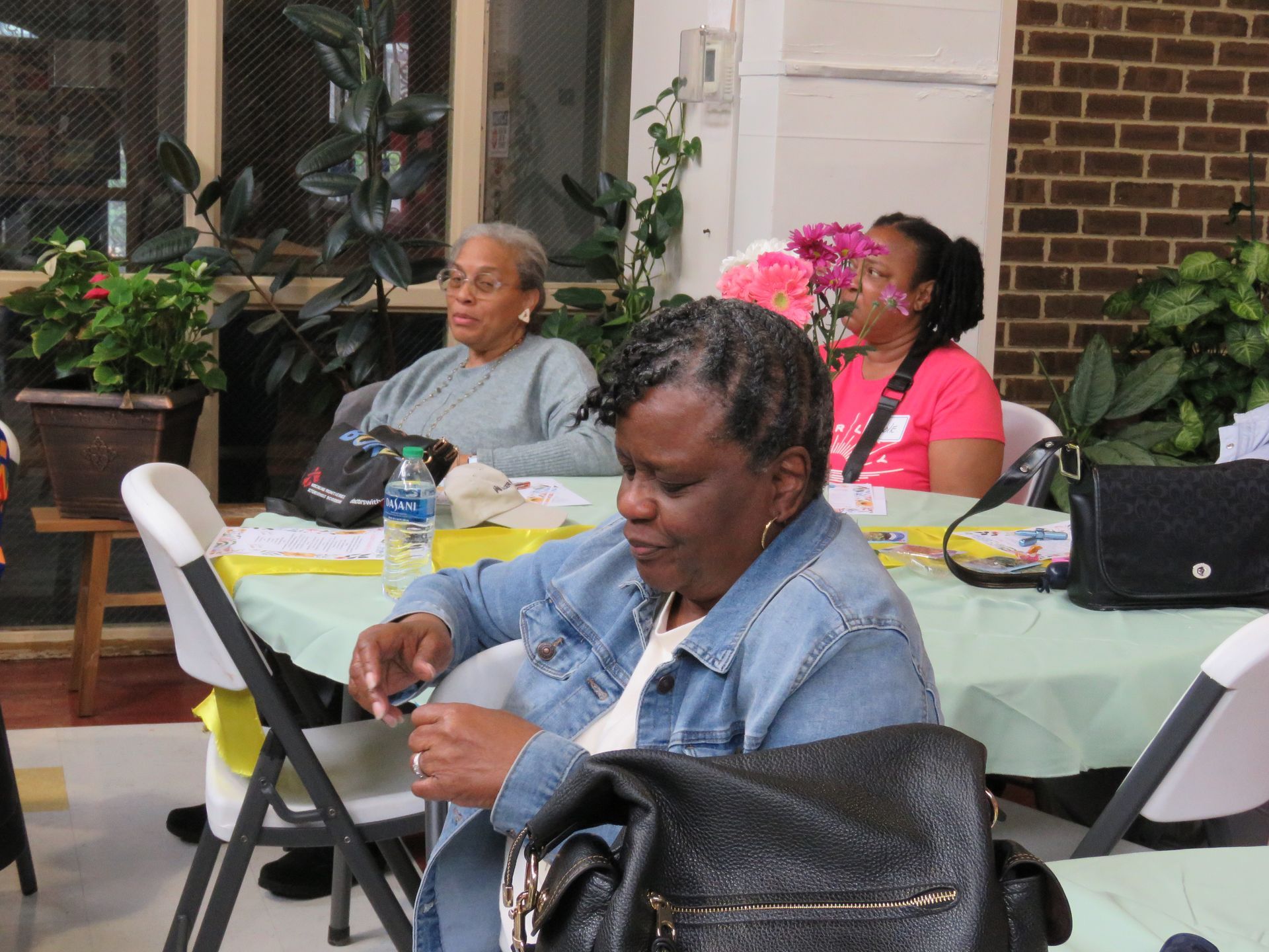 Three people seated at a table. One in a denim jacket, one in a light blue sweater, and one in a pink shirt.