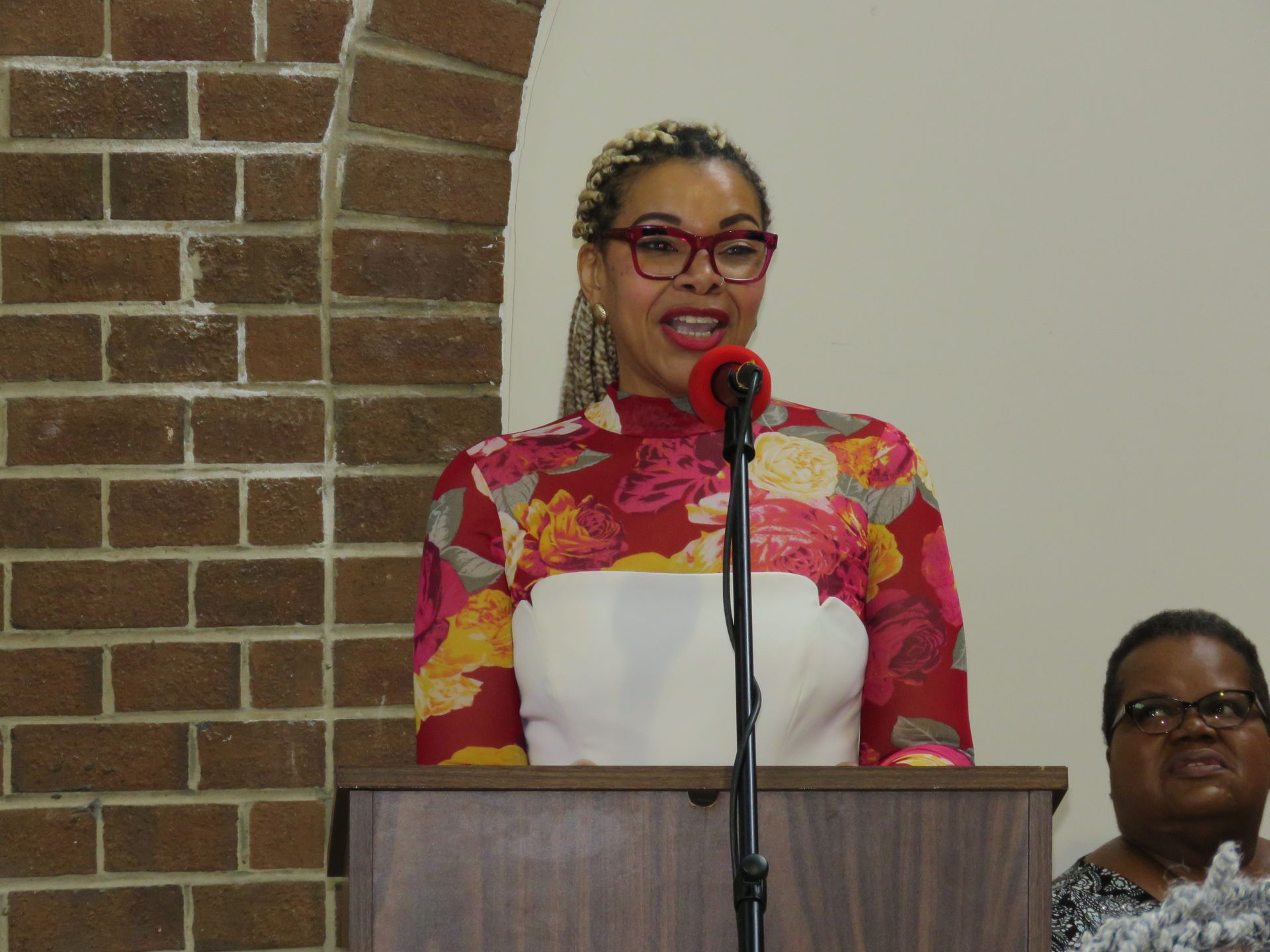 Woman speaking at a podium with a brick wall backdrop.