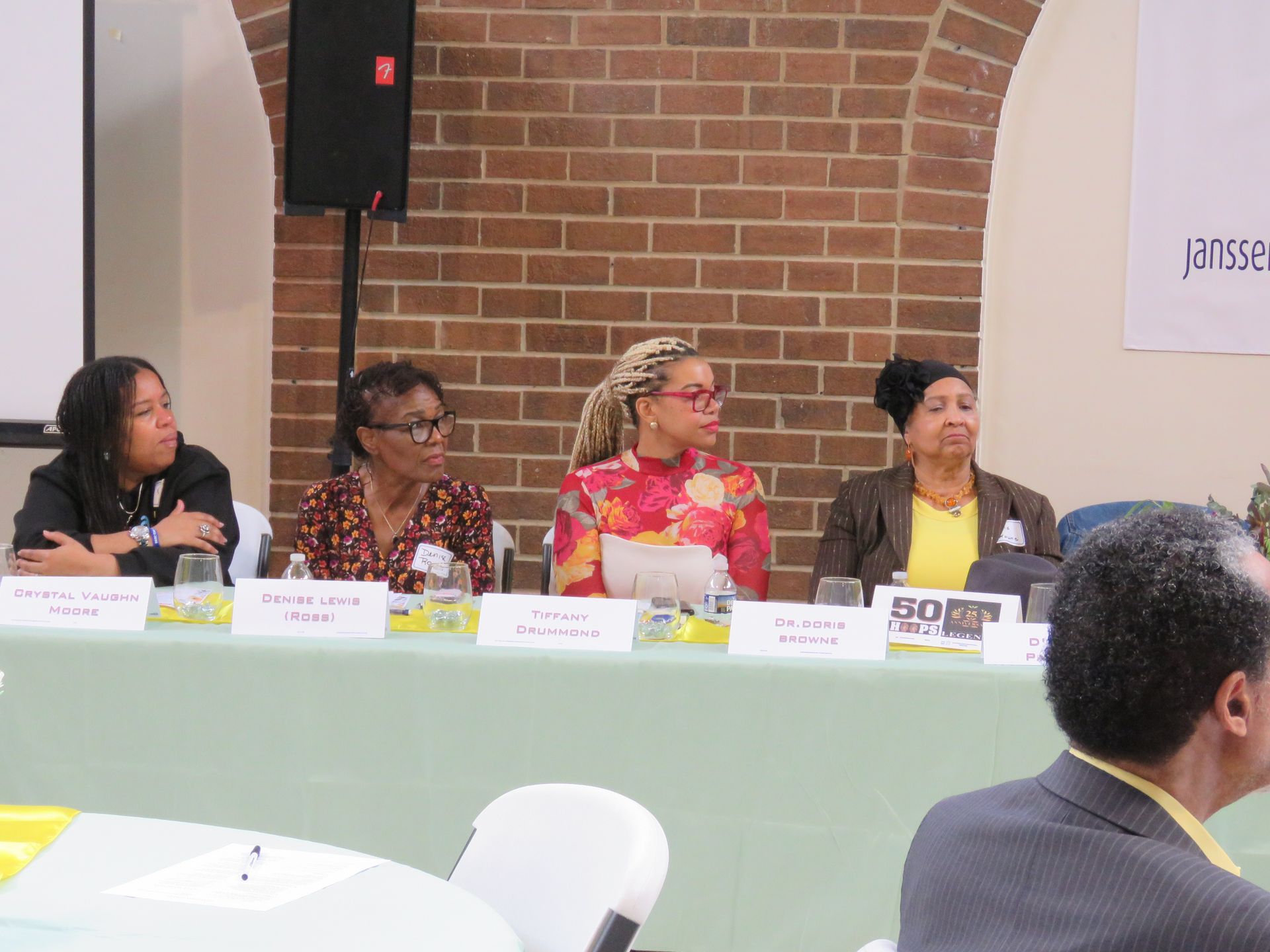 Panel of four women at a table, facing forward. Brick wall background.