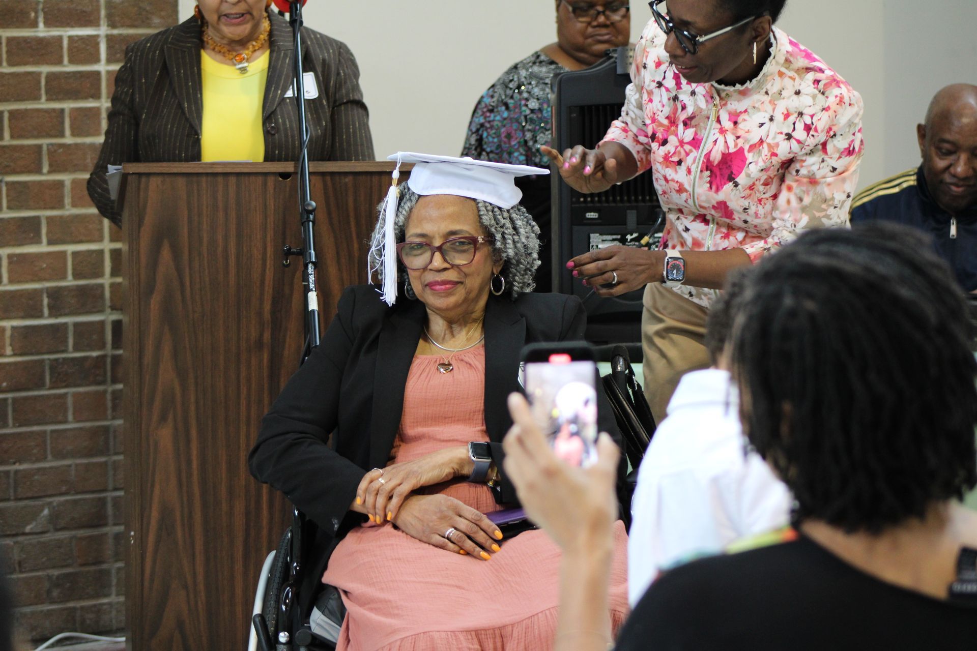 Woman in wheelchair gets her graduation cap adjusted at a ceremony.