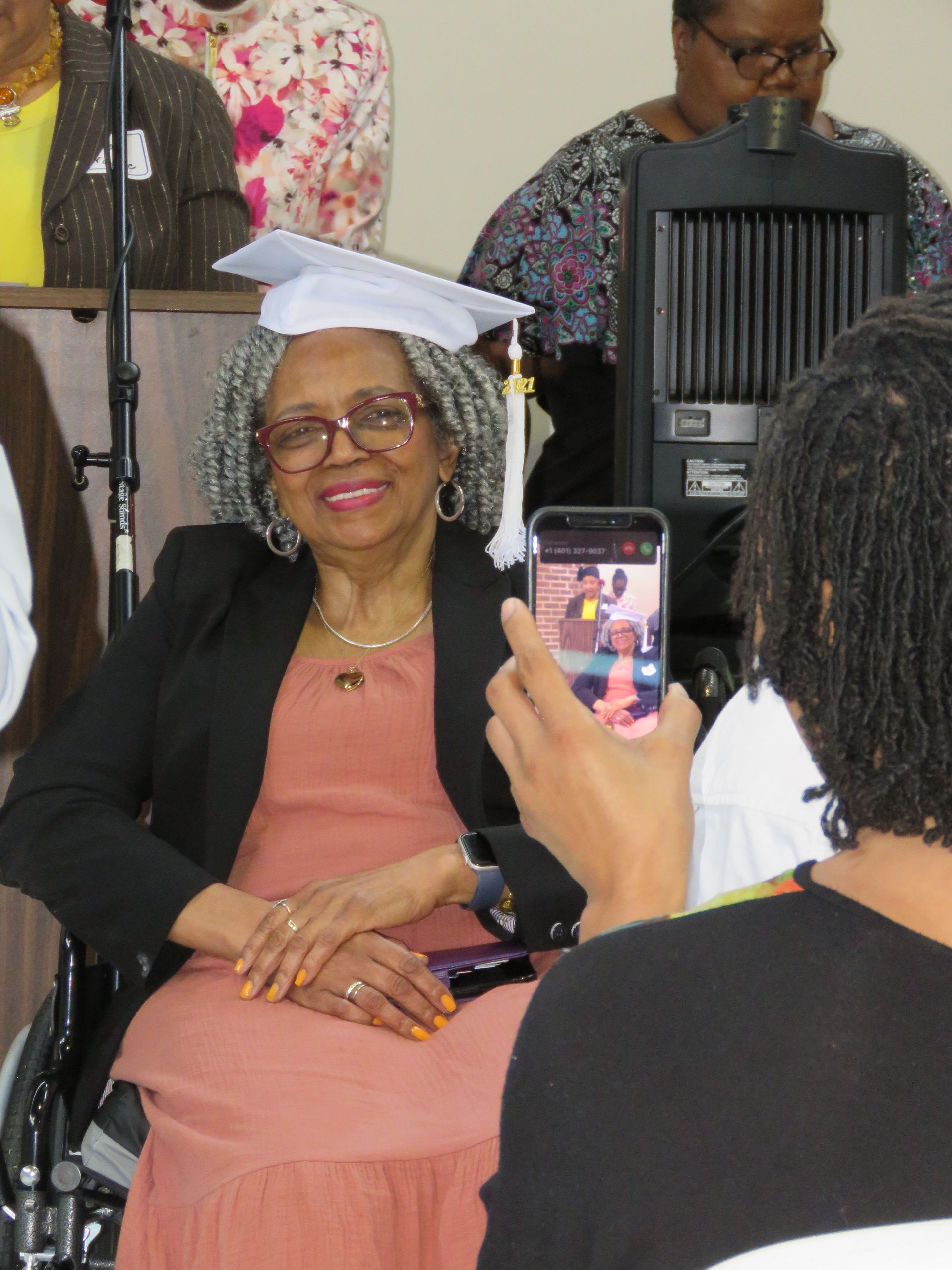 Older woman in graduation cap smiles while someone takes a photo of her.