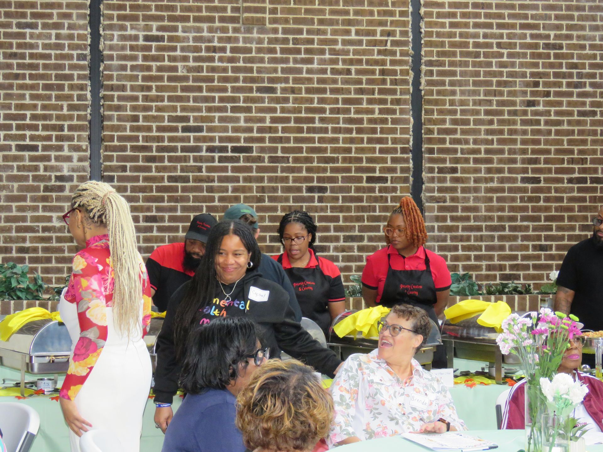 People at a catered event with a buffet table and brick wall background.
