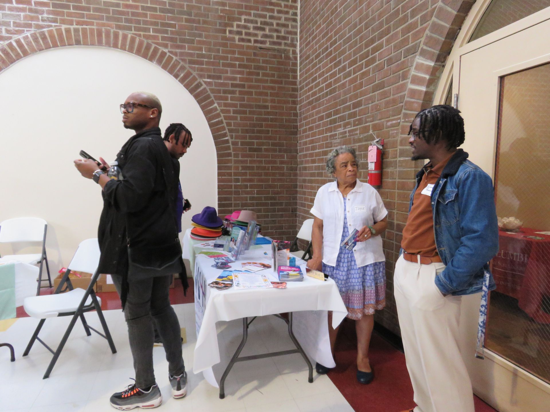 People at a table with brochures near a brick wall, chatting.