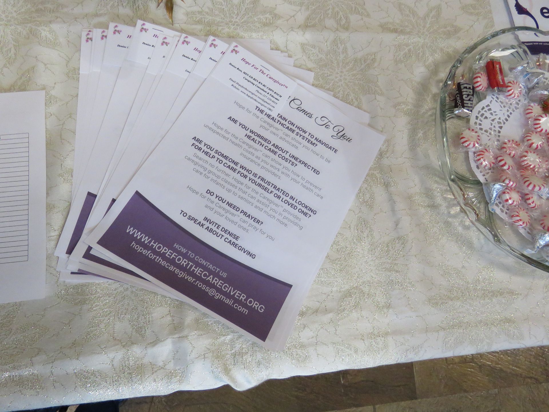 Stack of flyers with purple header, next to bowl of candies on a white cloth.