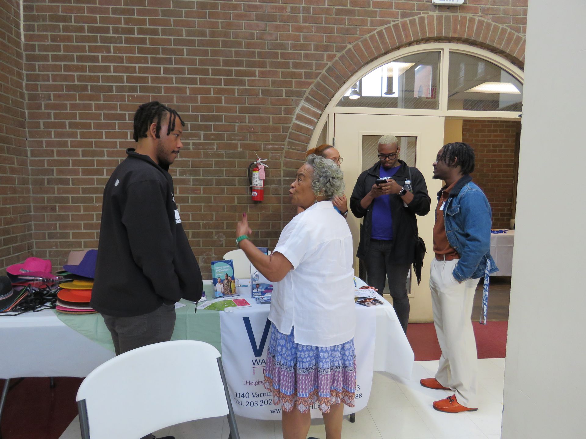 People at a table inside a brick building; one person gestures while speaking.