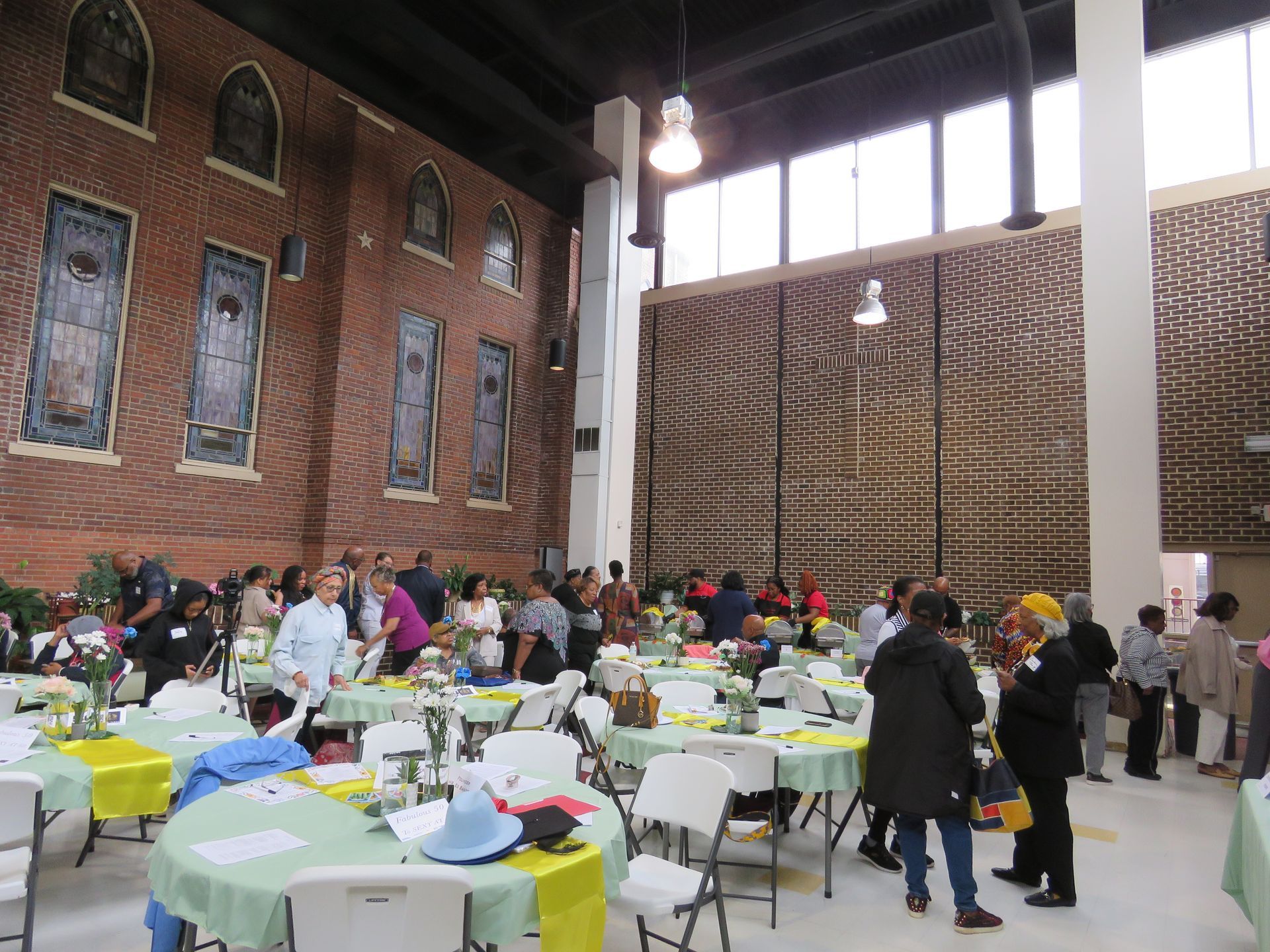 People gathered at tables in a large room with brick walls and tall windows.