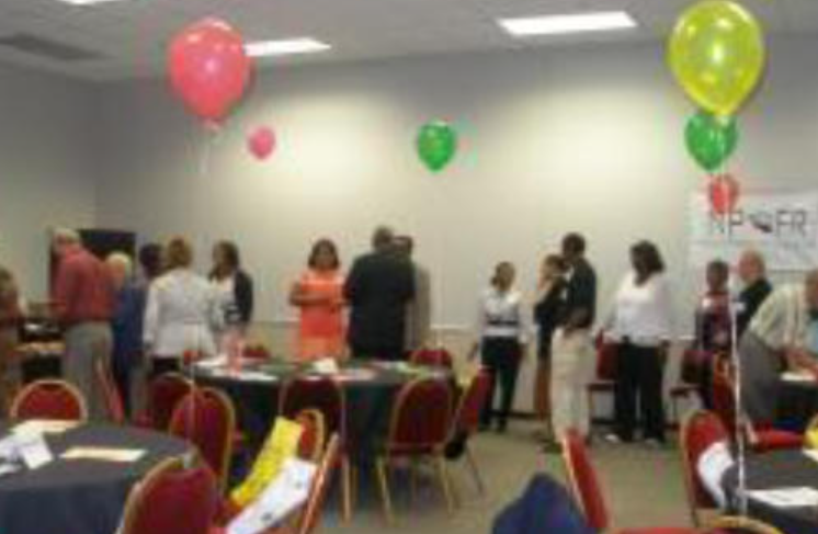 People gathering in a room with balloons and tables, likely an event or meeting.