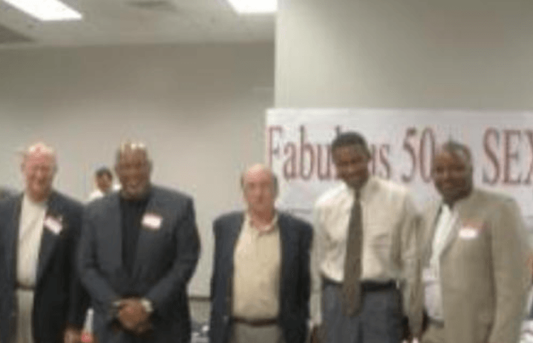 Five men in suits pose in front of a banner that reads 