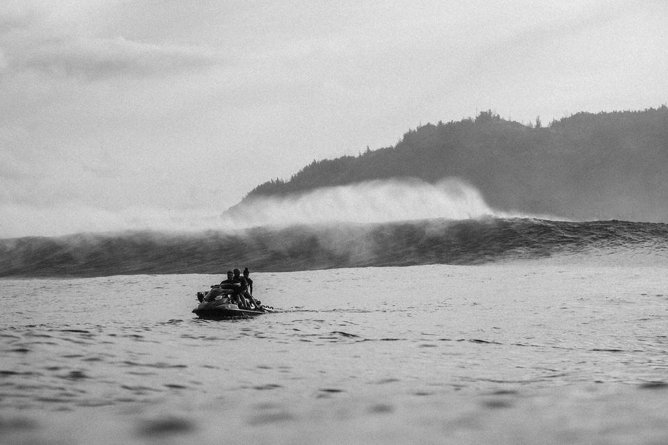 Small boat on calm water near a misty shoreline and forested hill under an overcast sky.
