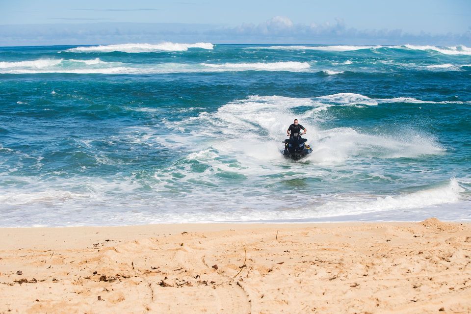 Person riding a jet ski through choppy blue waves near a sandy beach