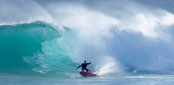 Surfer riding a red board inside a large turquoise wave