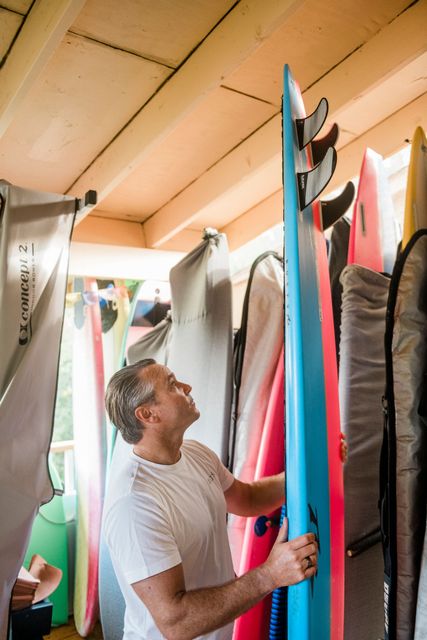 Person organizing colorful surfboards in a storage shed under a wooden roof.