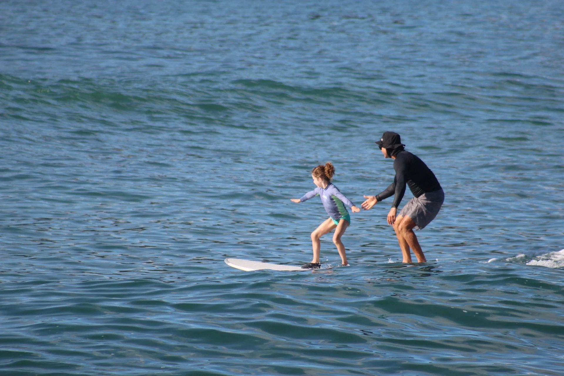 Adult helping child balance on a surfboard in the ocean