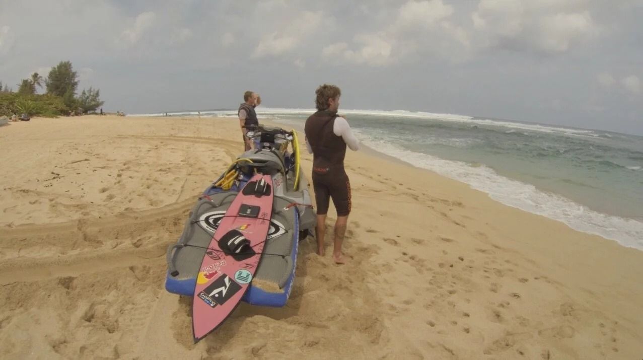 Surfboards on a sandy beach with two people standing by the shoreline and waves rolling in