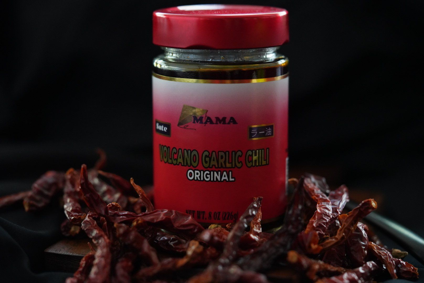 A jar of beans garlic chili is sitting on top of a pile of dried red peppers.