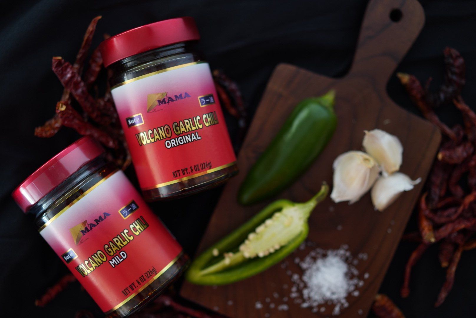 Two jars of sauce are sitting on top of a wooden cutting board.