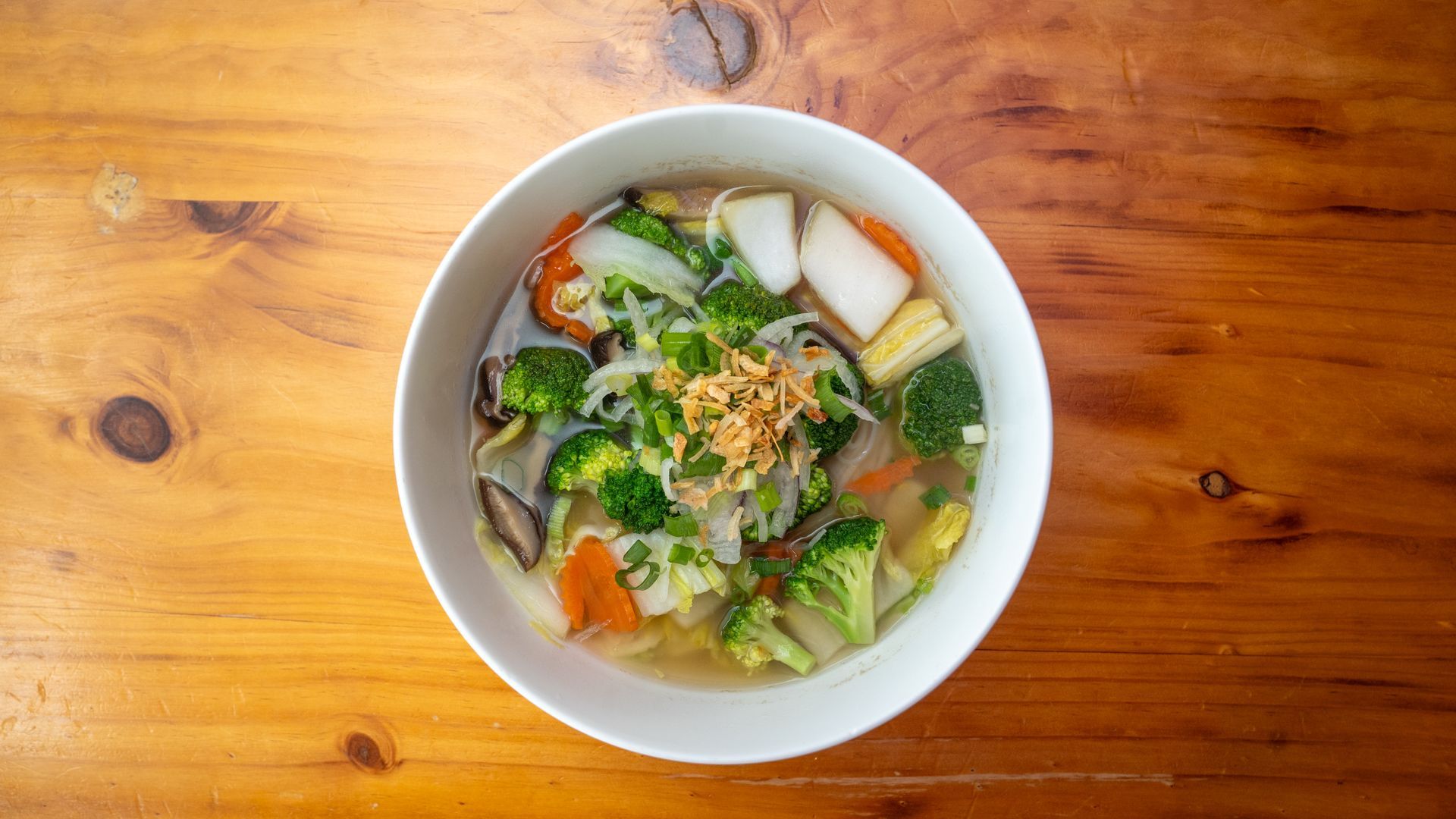 A bowl of vegetable soup is sitting on a wooden table.
