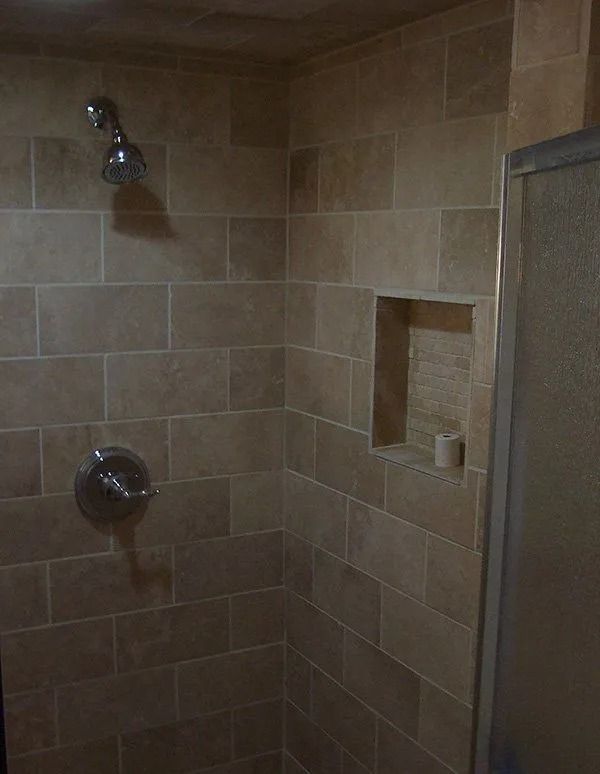 A shower with a shower head and a shelf in the corner.