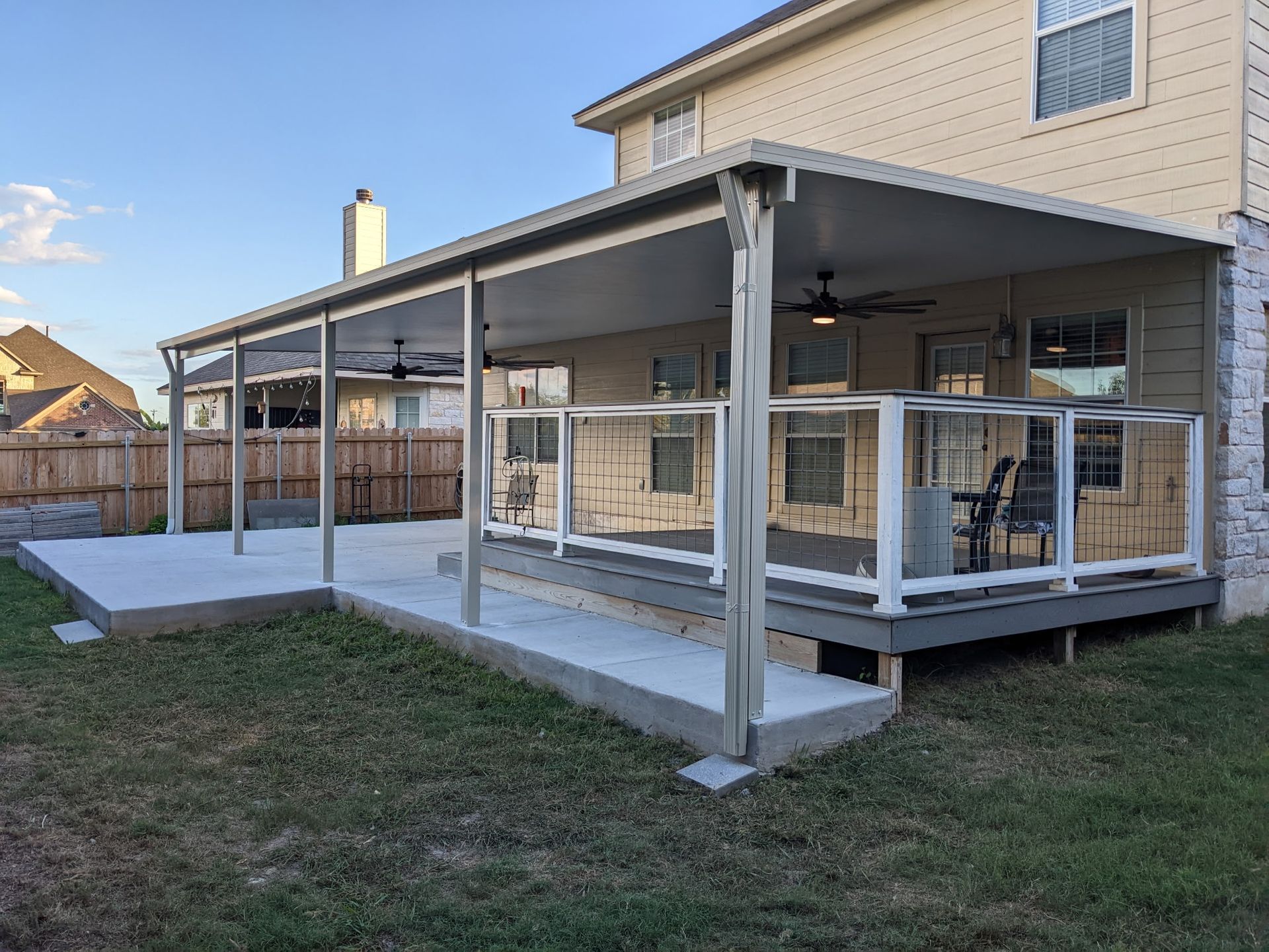 A large covered deck with a glass railing is in the backyard of a house.