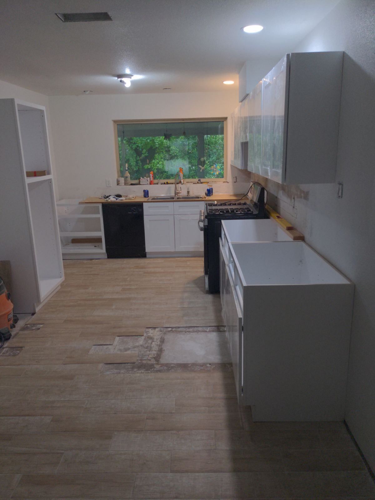 A kitchen with white cabinets , a stove , a sink , and a window.