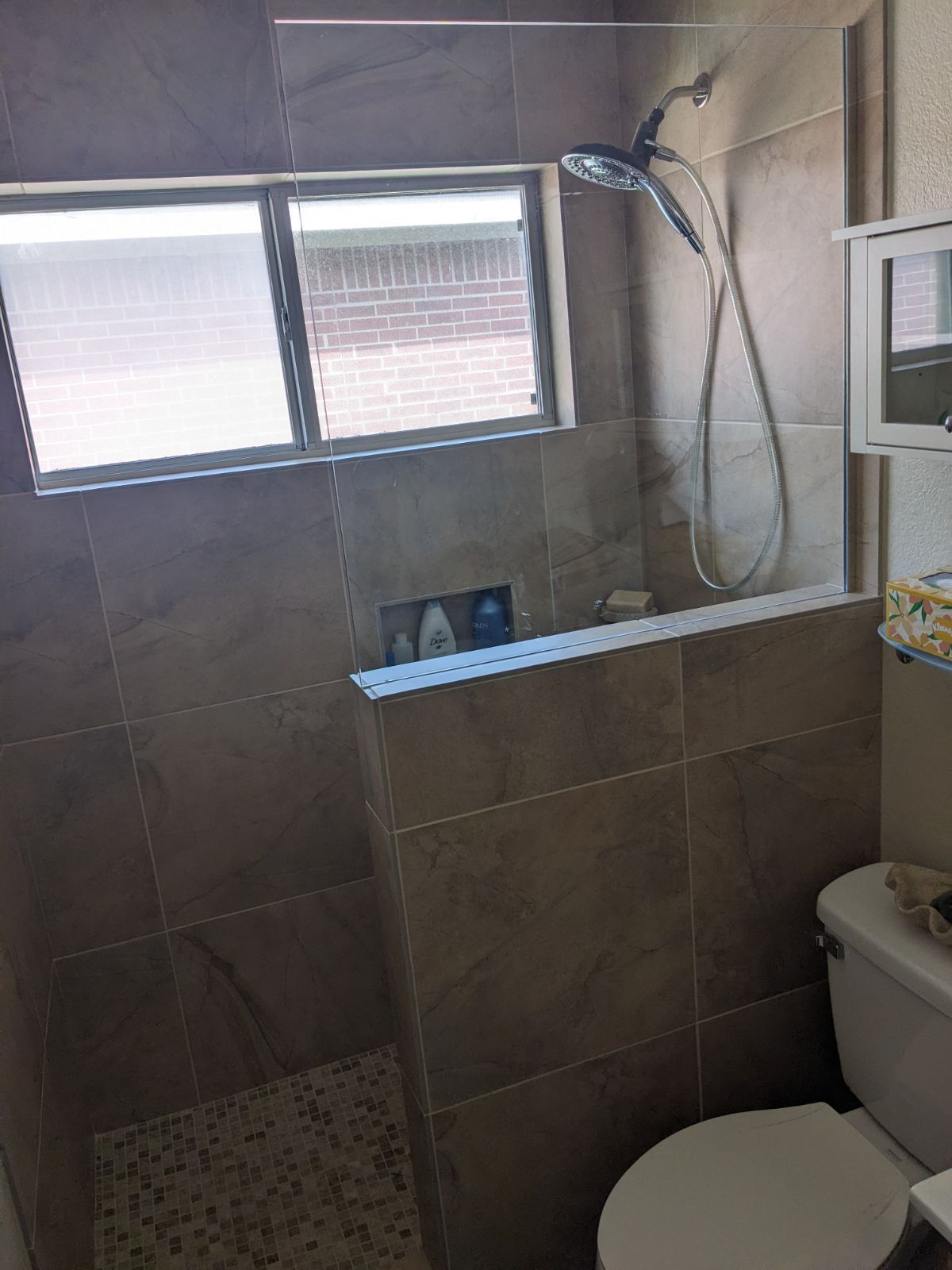 A bathroom with a toilet , shower and window.