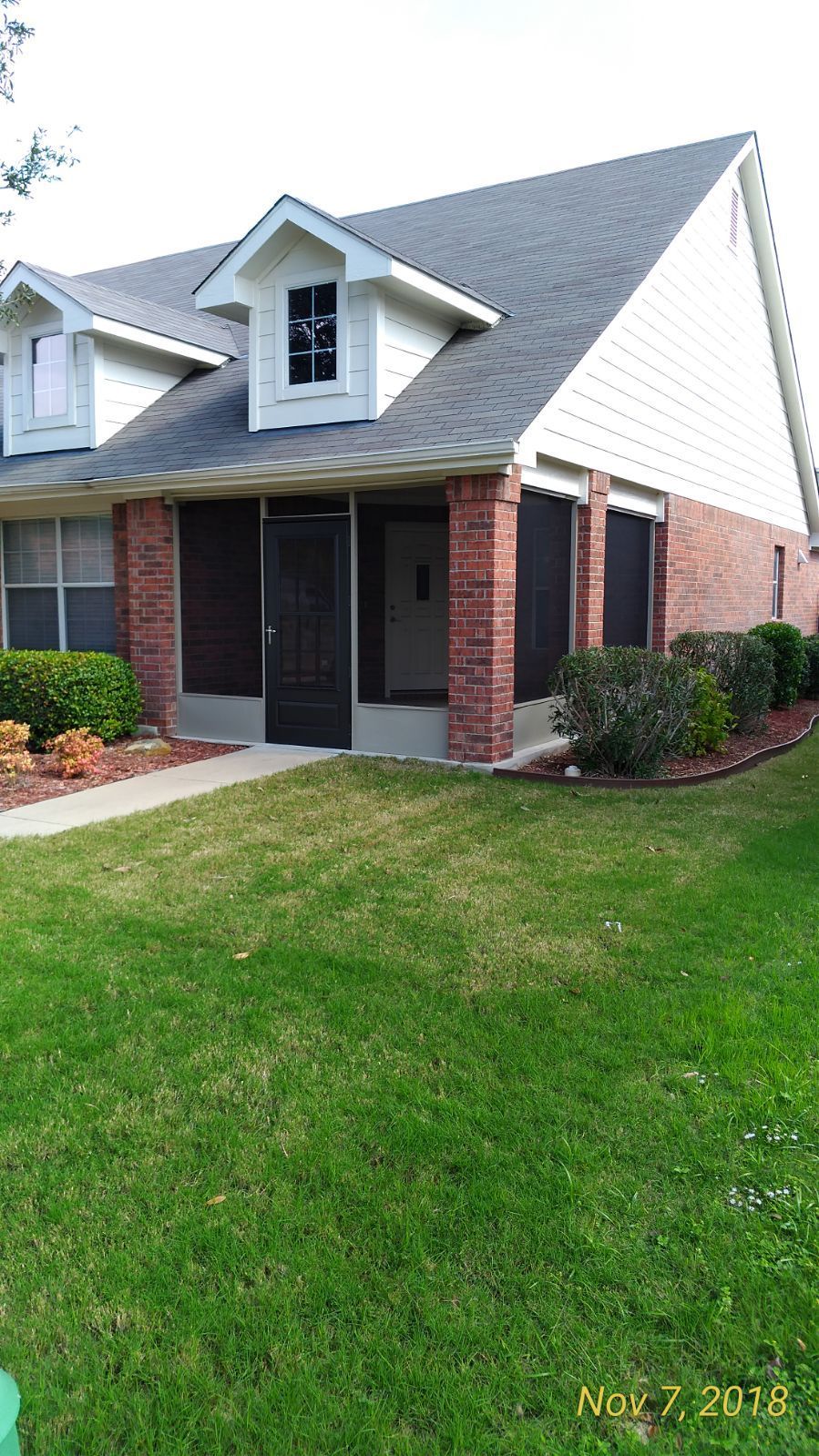 A house with a screened in porch and a lush green lawn.