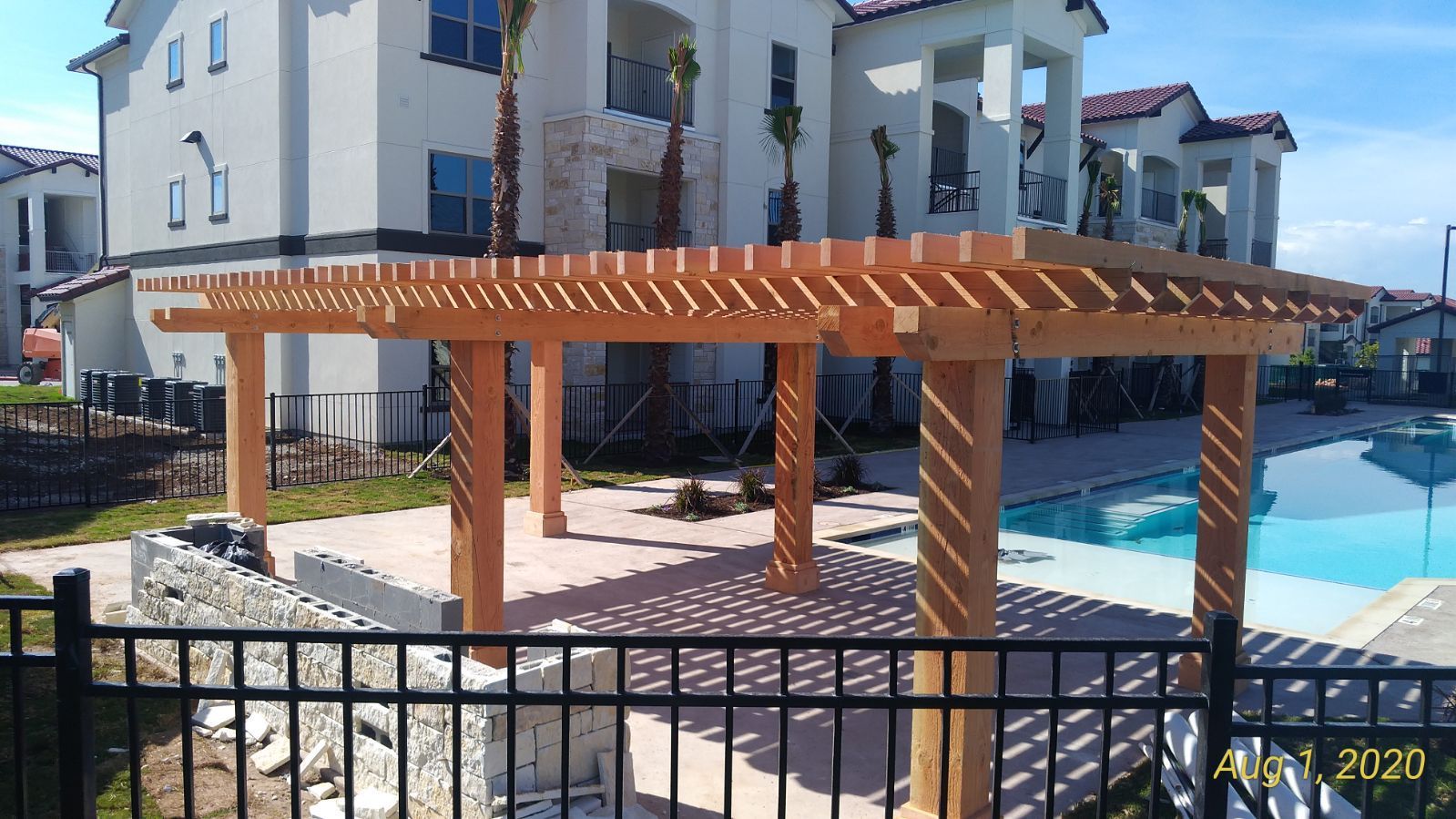 A wooden pergola is sitting next to a pool in front of a large building.