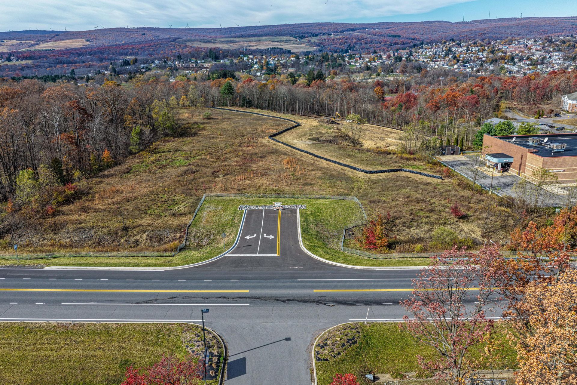 Aerial view of a road leading to a clearing in a wooded area. Brown and green landscape with a blue sky.