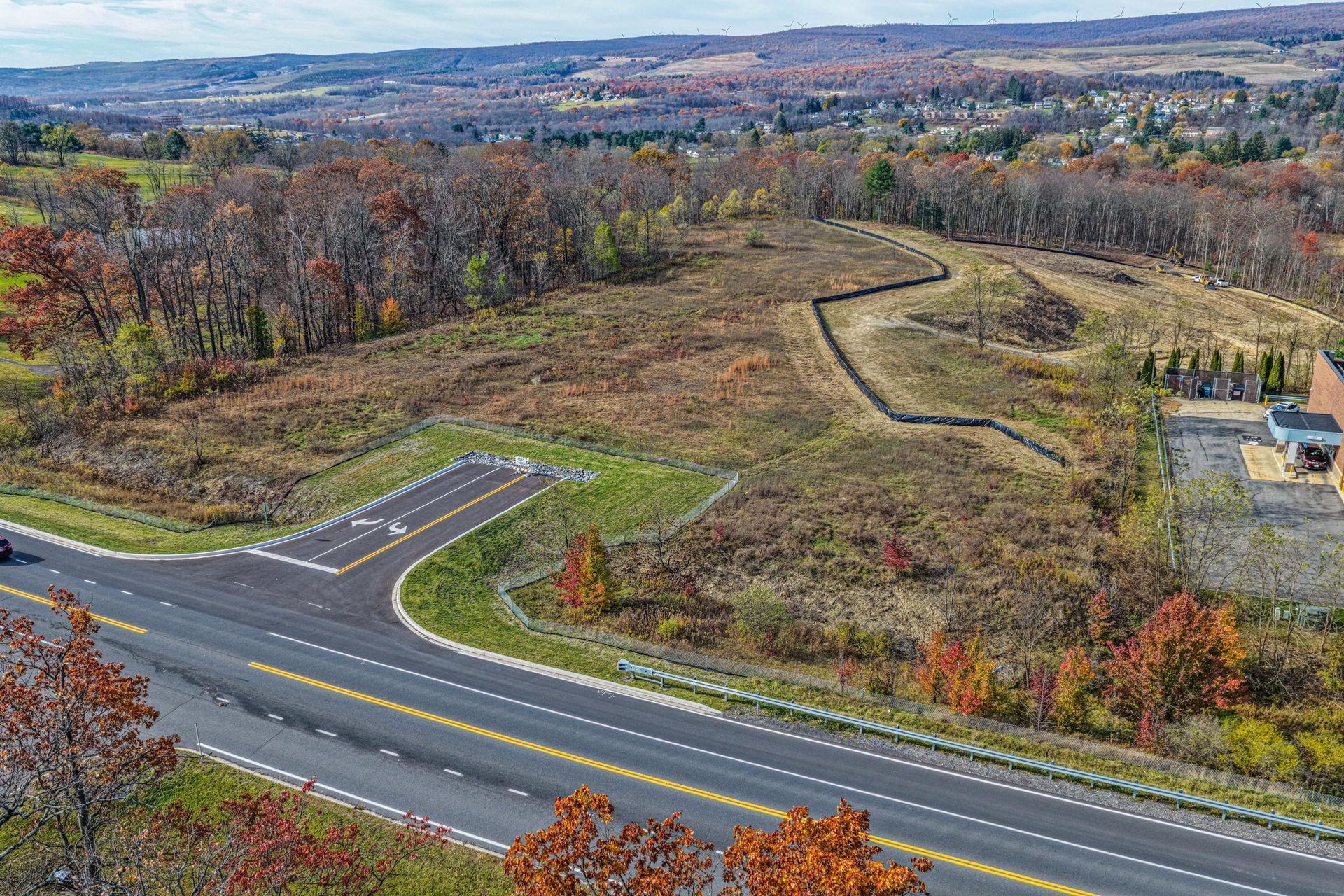 Aerial view of a cleared plot of land with a newly paved road and fall foliage.