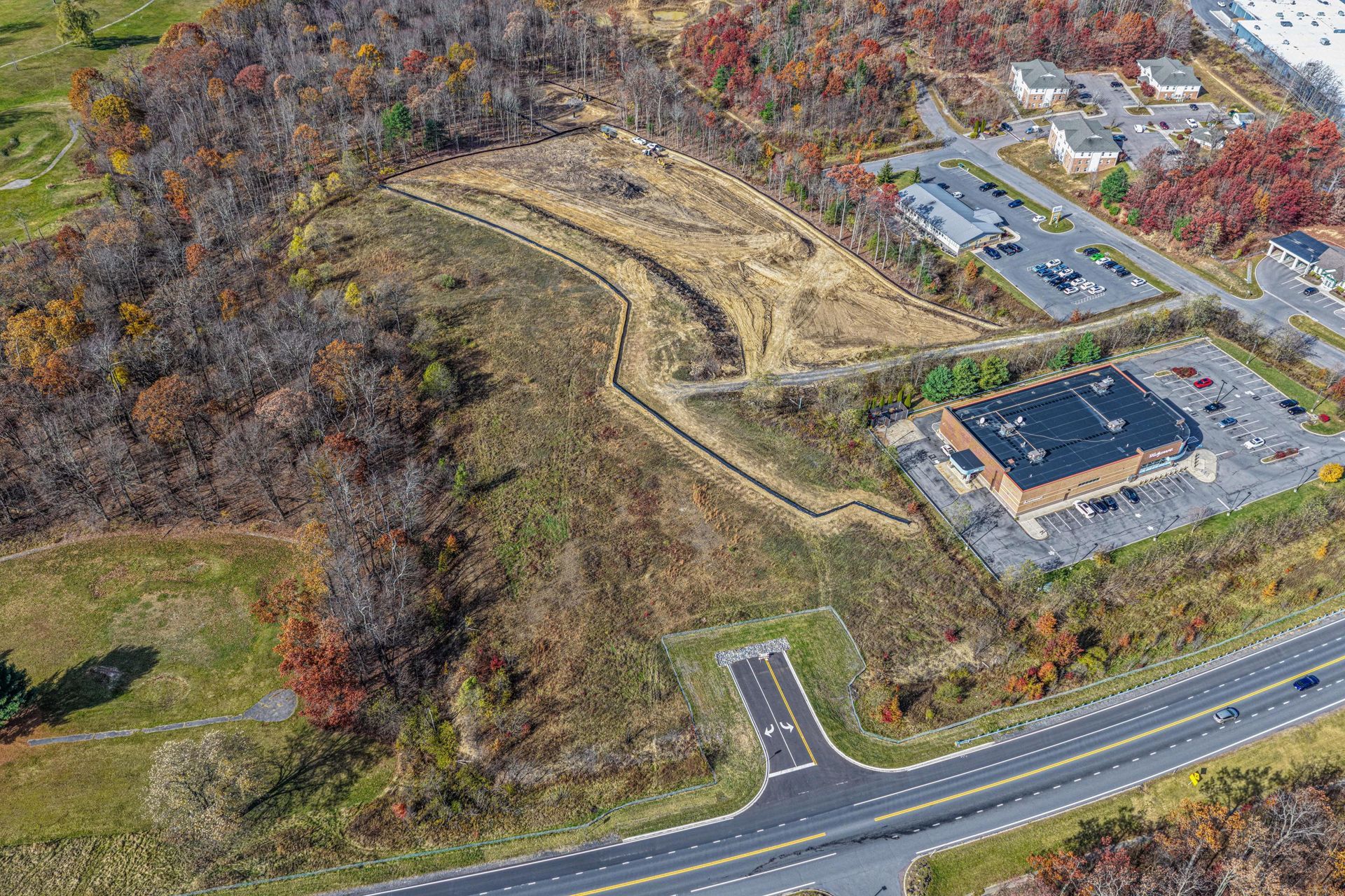 Aerial view of a cleared construction site next to a commercial building, road, and residential area.