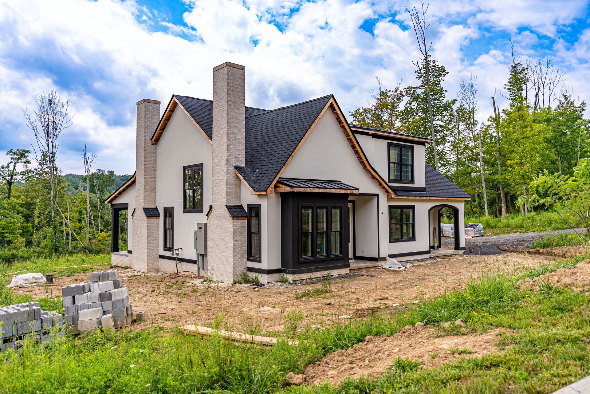 Newly constructed house with white stucco, black trim, and a black roof, set in a grassy.