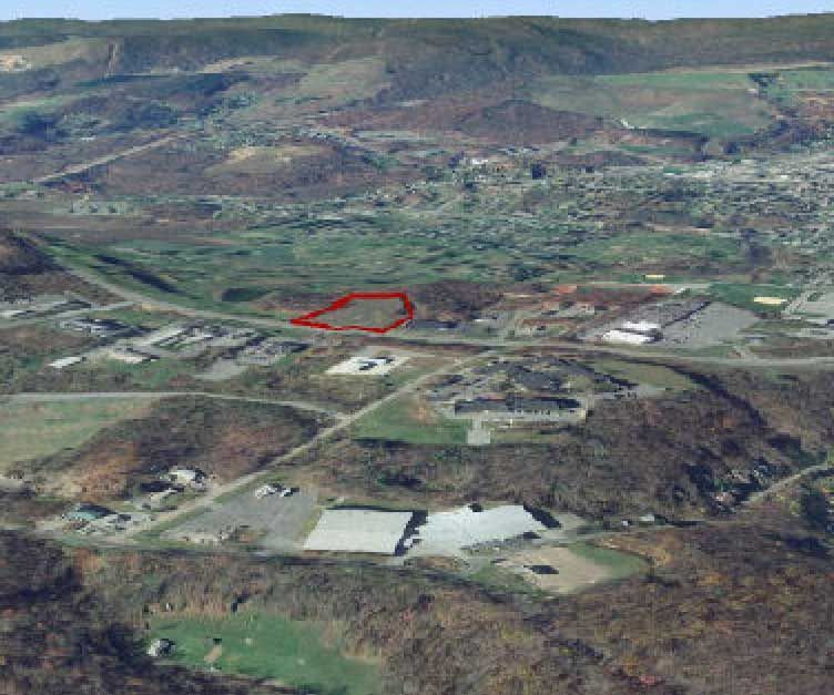 Aerial view of a landscape with a red polygon highlighting a plot of land, with buildings and roads in the foreground.