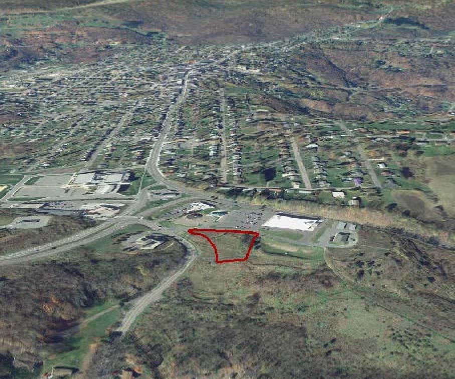 Aerial view of a town, with a red outline highlighting a vacant lot in the foreground, next to a road.