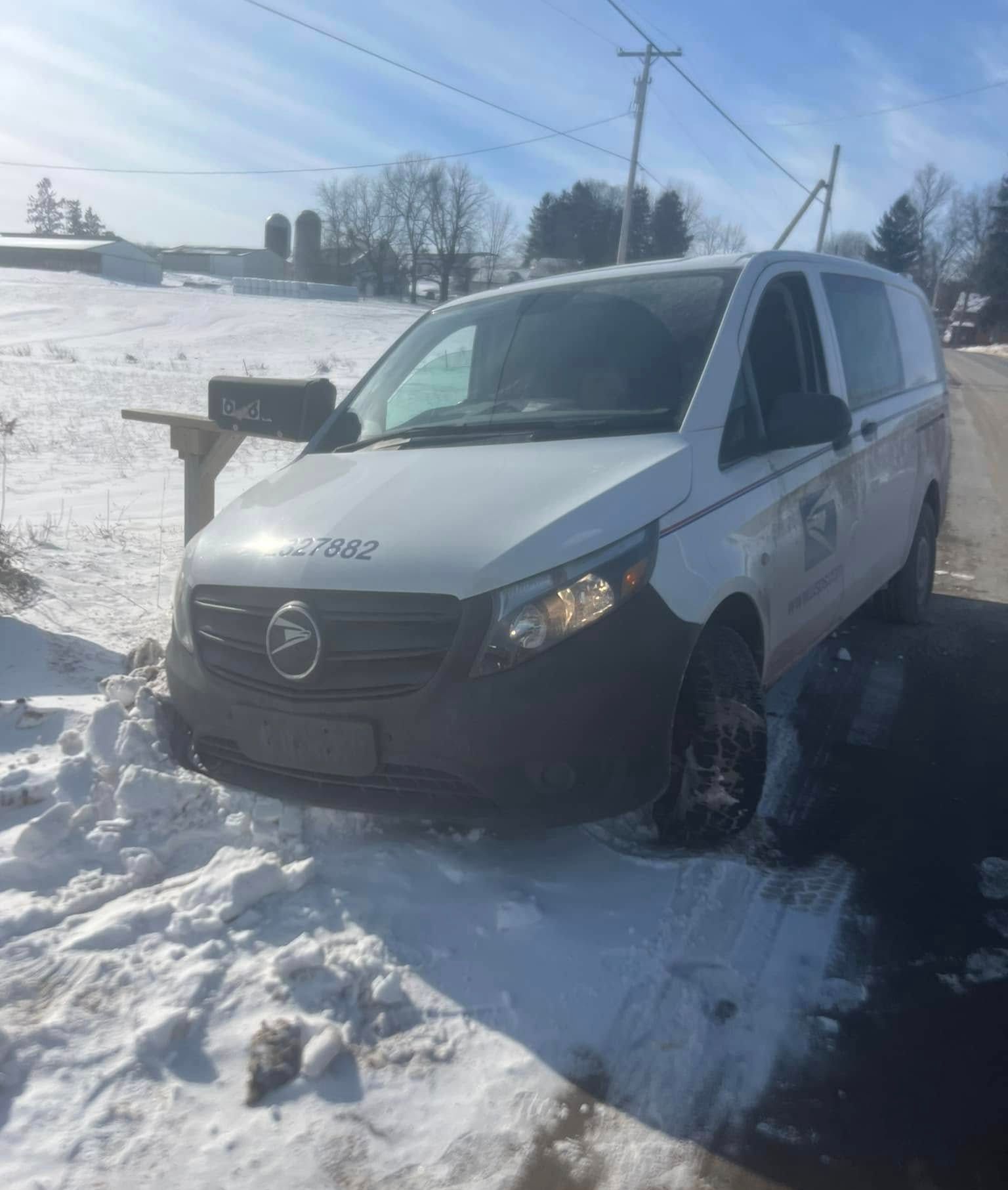A white van is parked in the snow next to a mailbox.