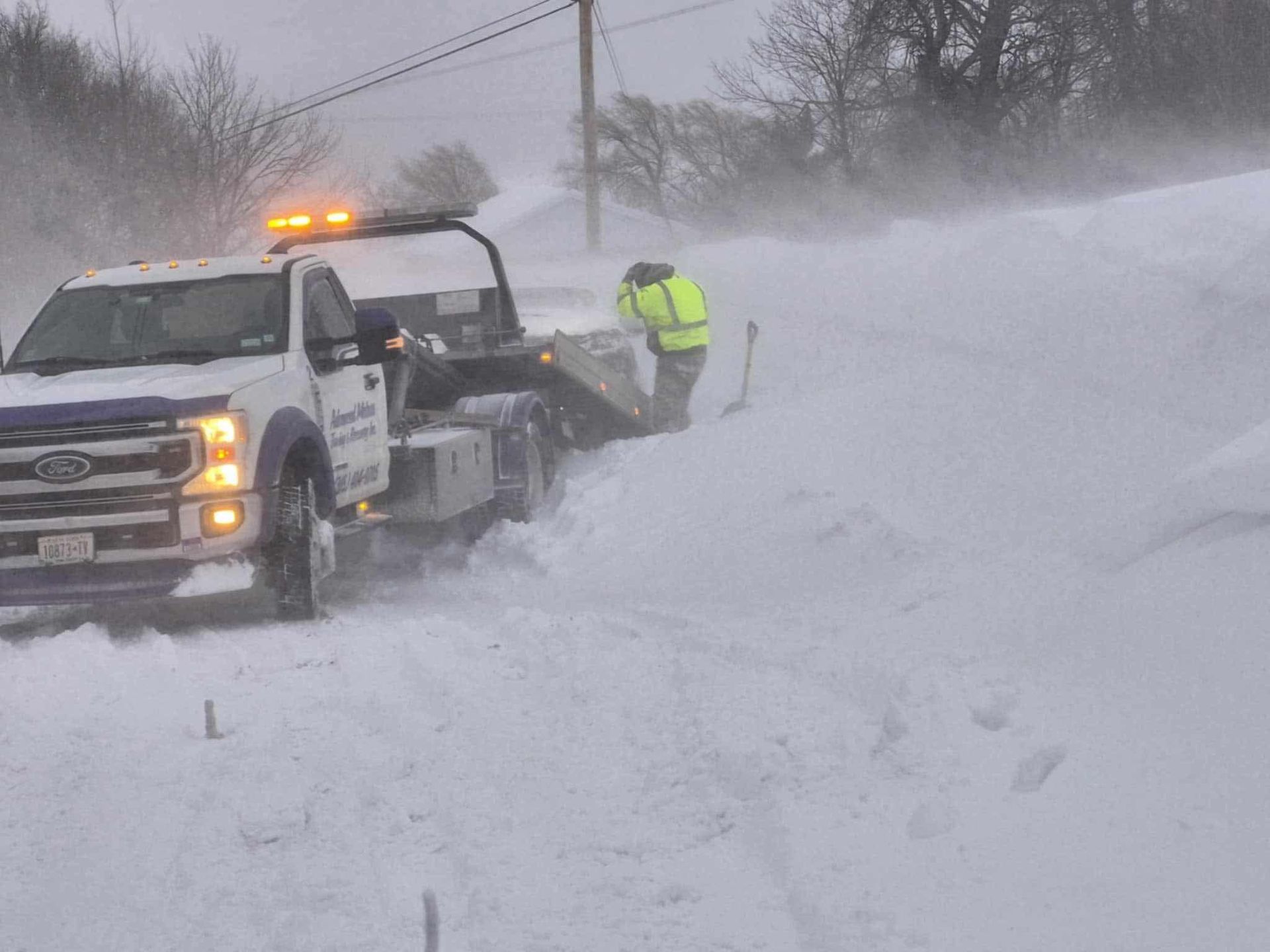A tow truck is driving down a snow covered road.