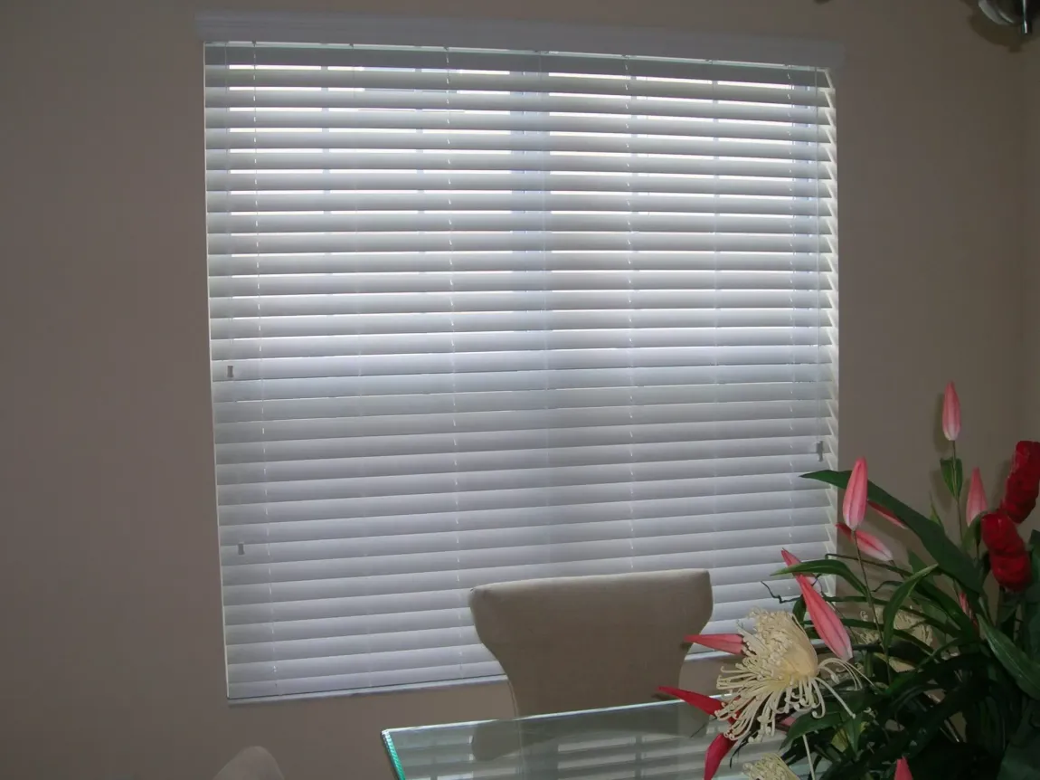 White window blinds with sunlight filtering through and a pull cord on the left side