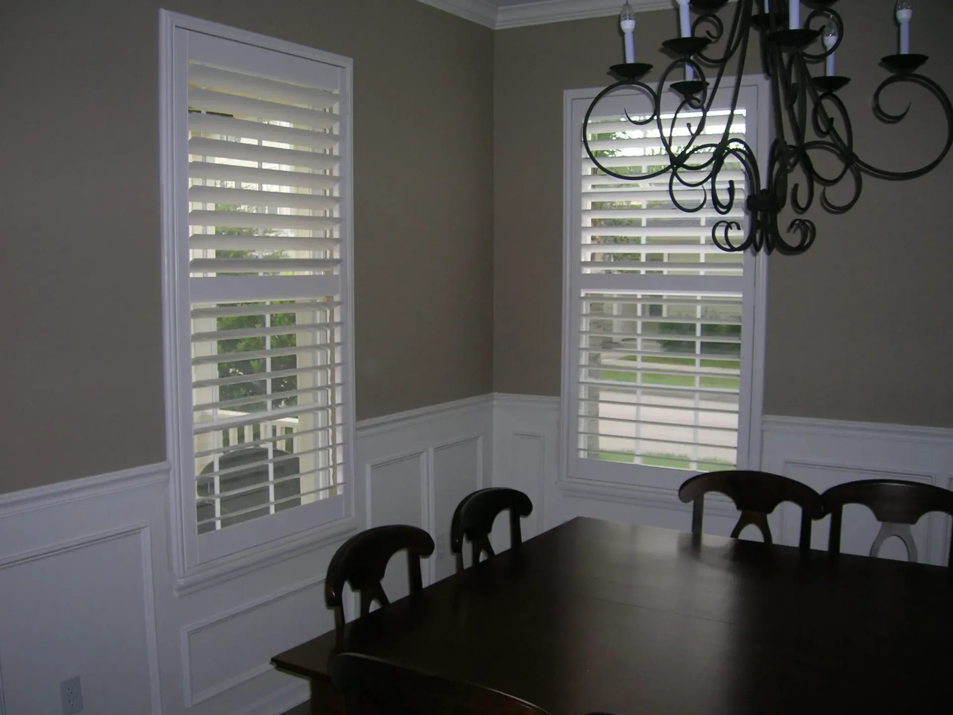 Dining room with dark table, chandelier, and windows with white shutters on beige walls