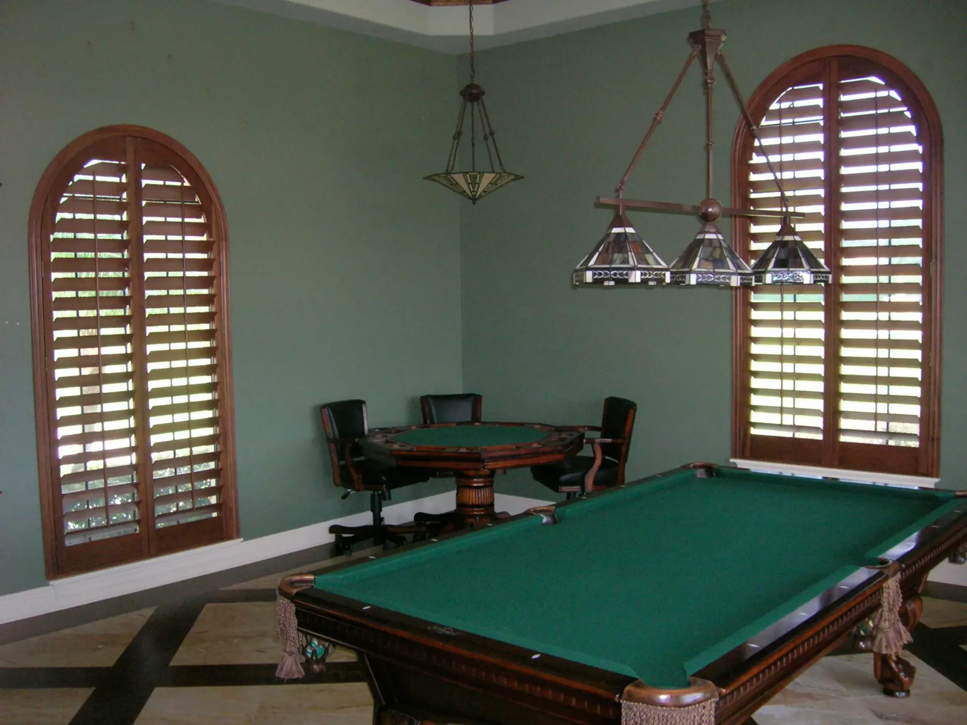 Game room with green pool table, arched windows, and seating area.