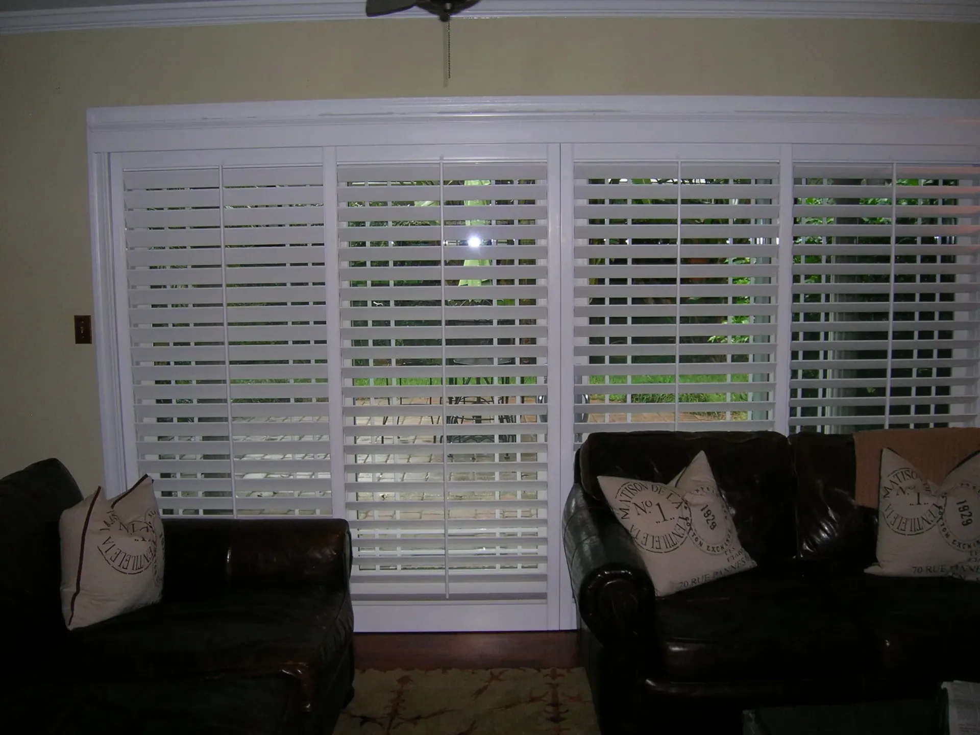 Living room with large white plantation shutters, flanked by two dark sofas and decorative pillows.