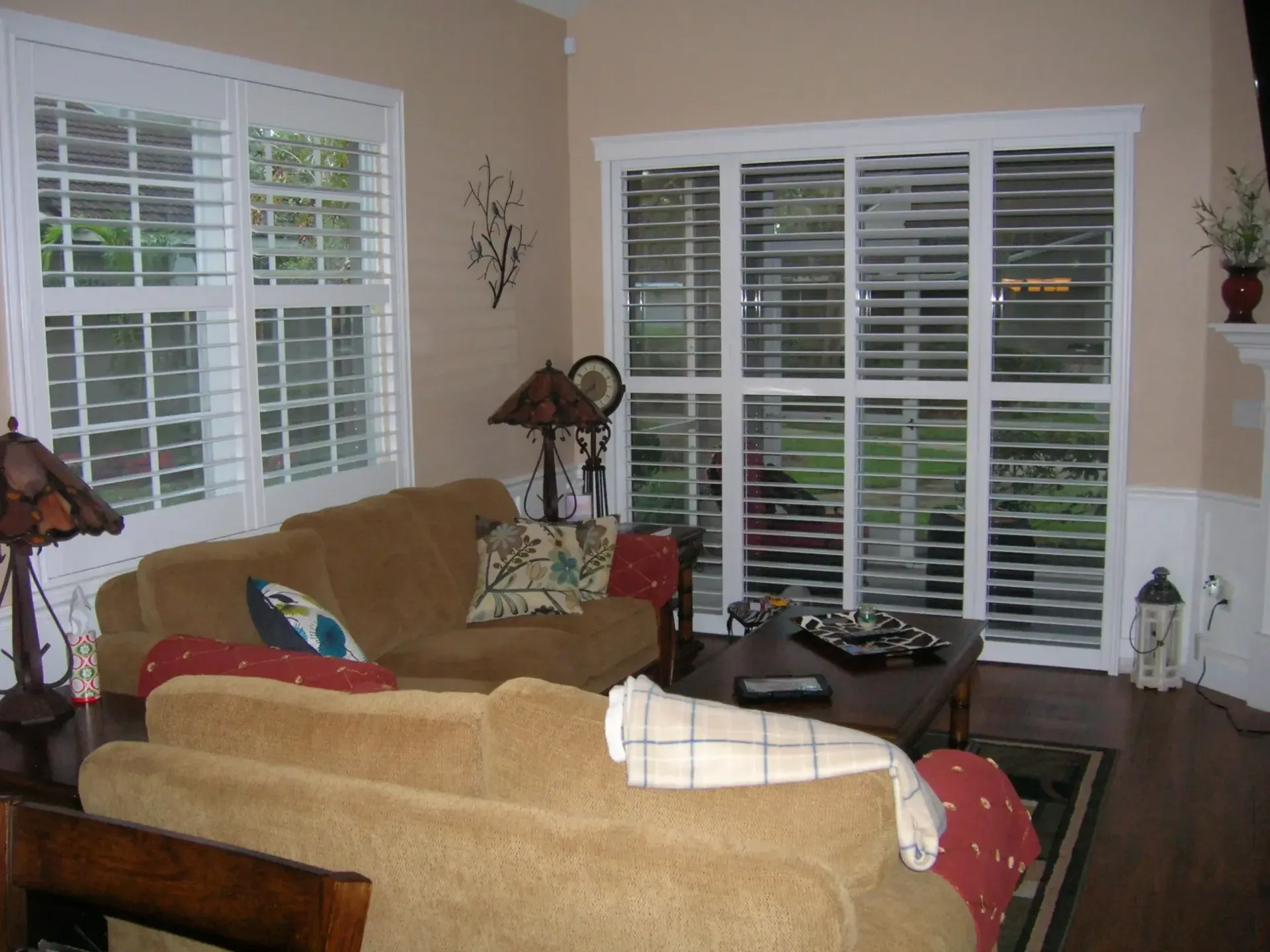 Living room with beige sofas, lamps, and large windows with white blinds