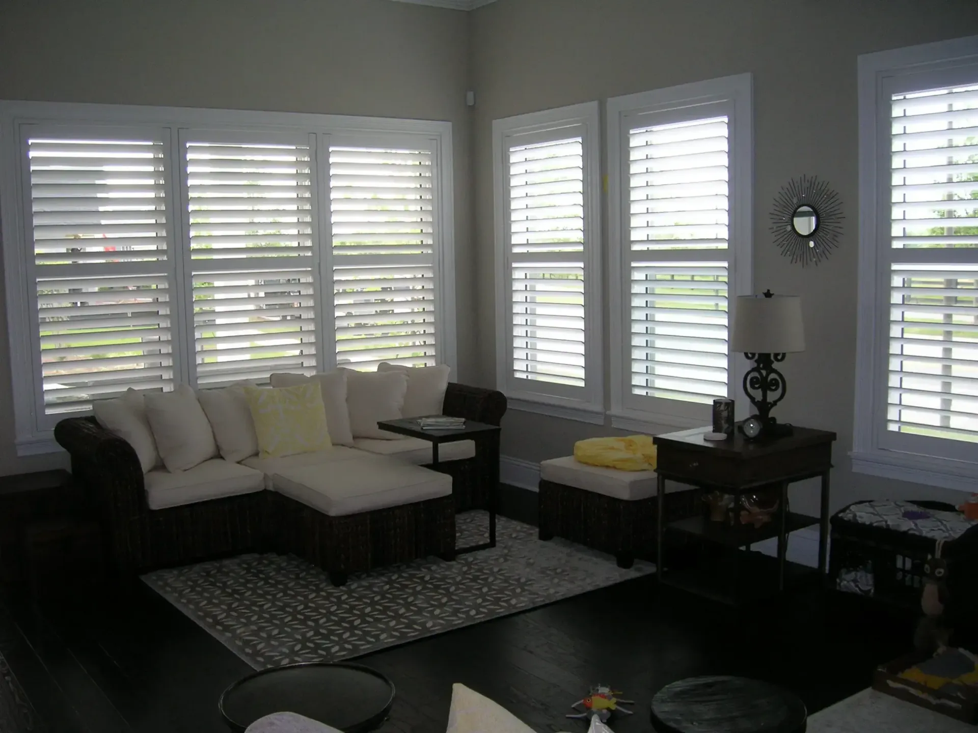 Living room with dark sofa, white shutters, rug, and side table with lamp
