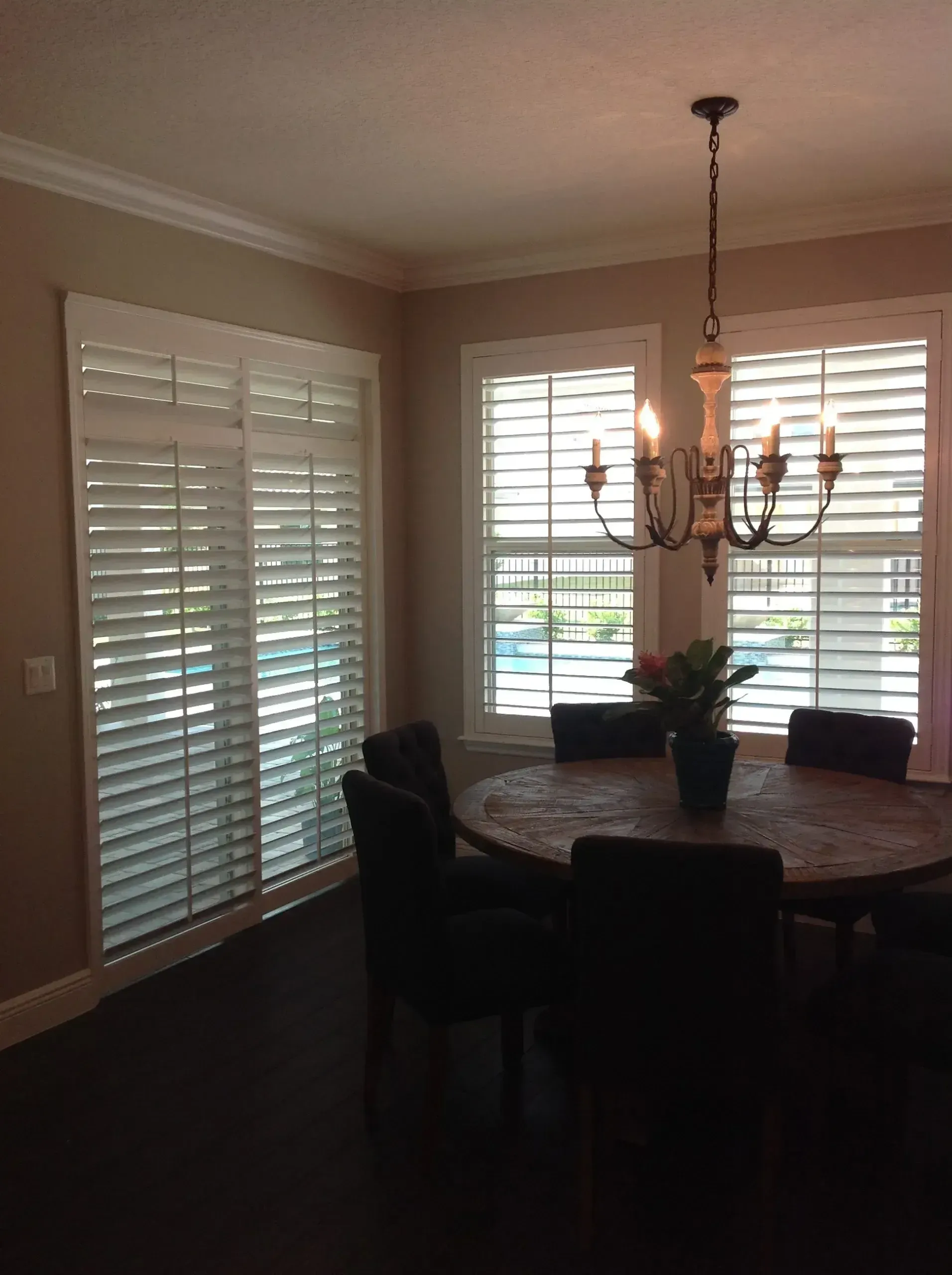 Dining room with round table, dark chairs, chandelier, and plantation shutters letting in daylight
